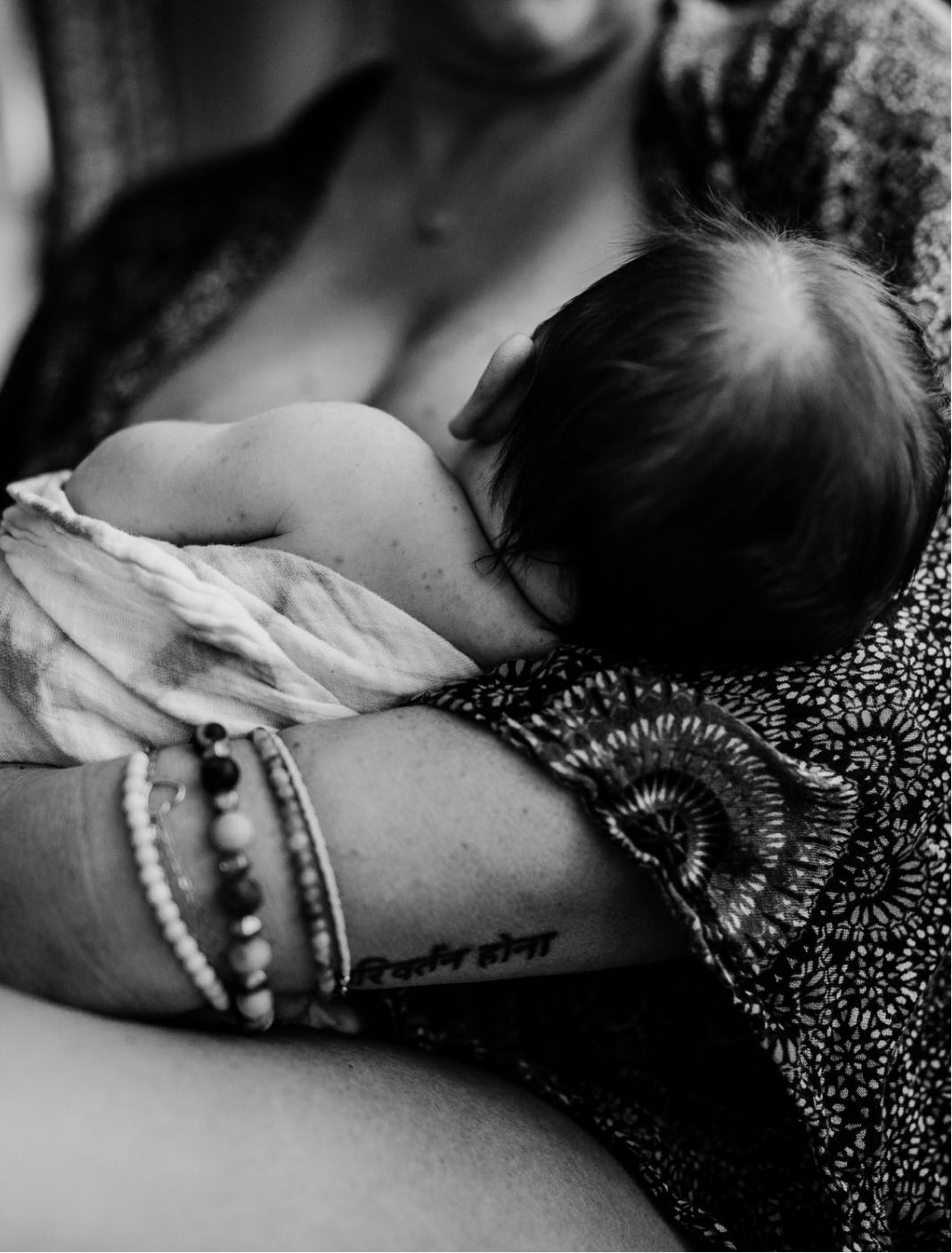 Black and white photo of a mother holding a newborn close while breastfeeding, capturing quiet bonding, skin-to-skin contact, and nurturing infant care