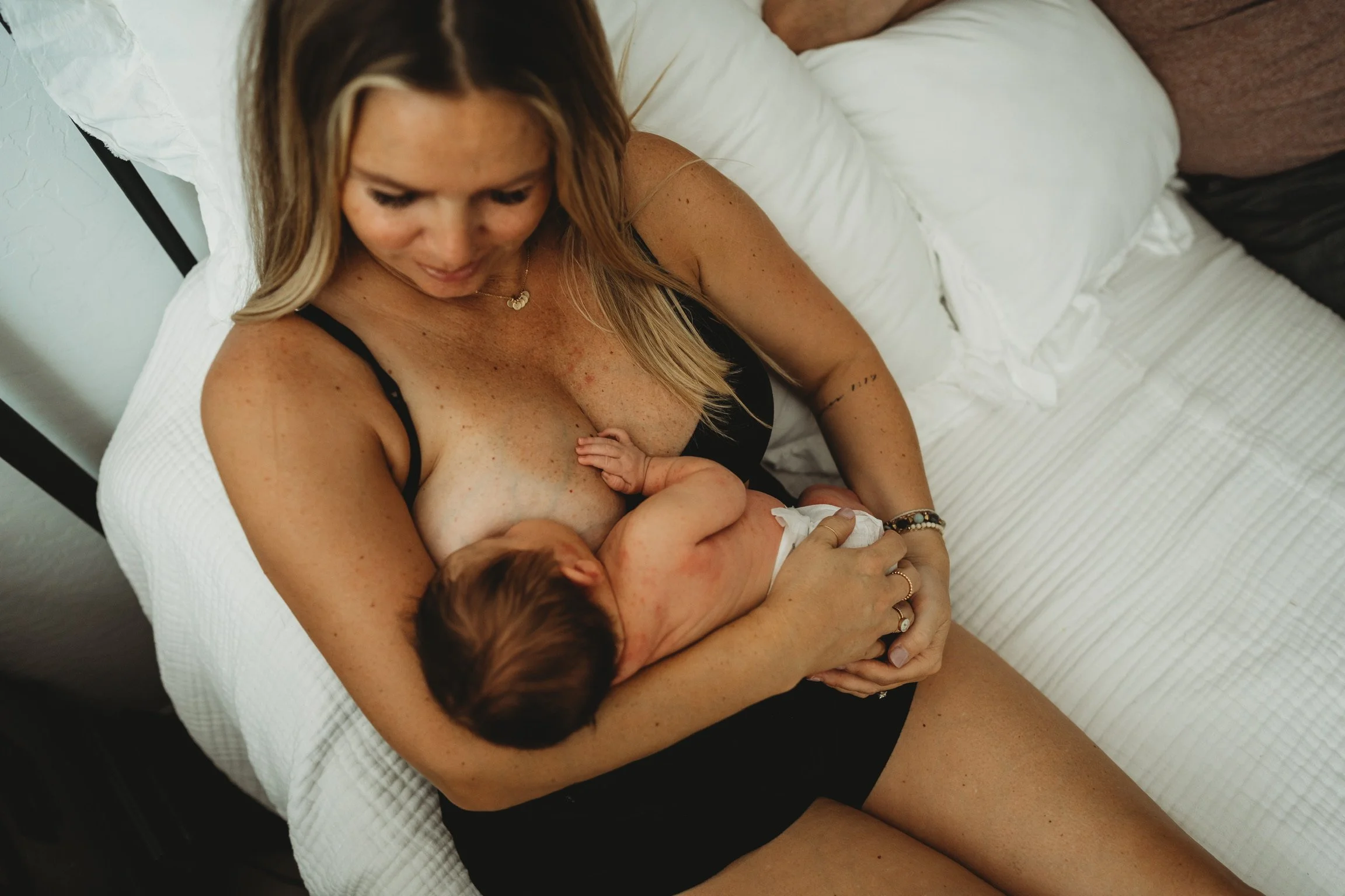 Mother breastfeeding a newborn baby while resting on a bed, capturing a calm bonding moment that highlights infant nourishment, skin-to-skin contact, and early maternal care