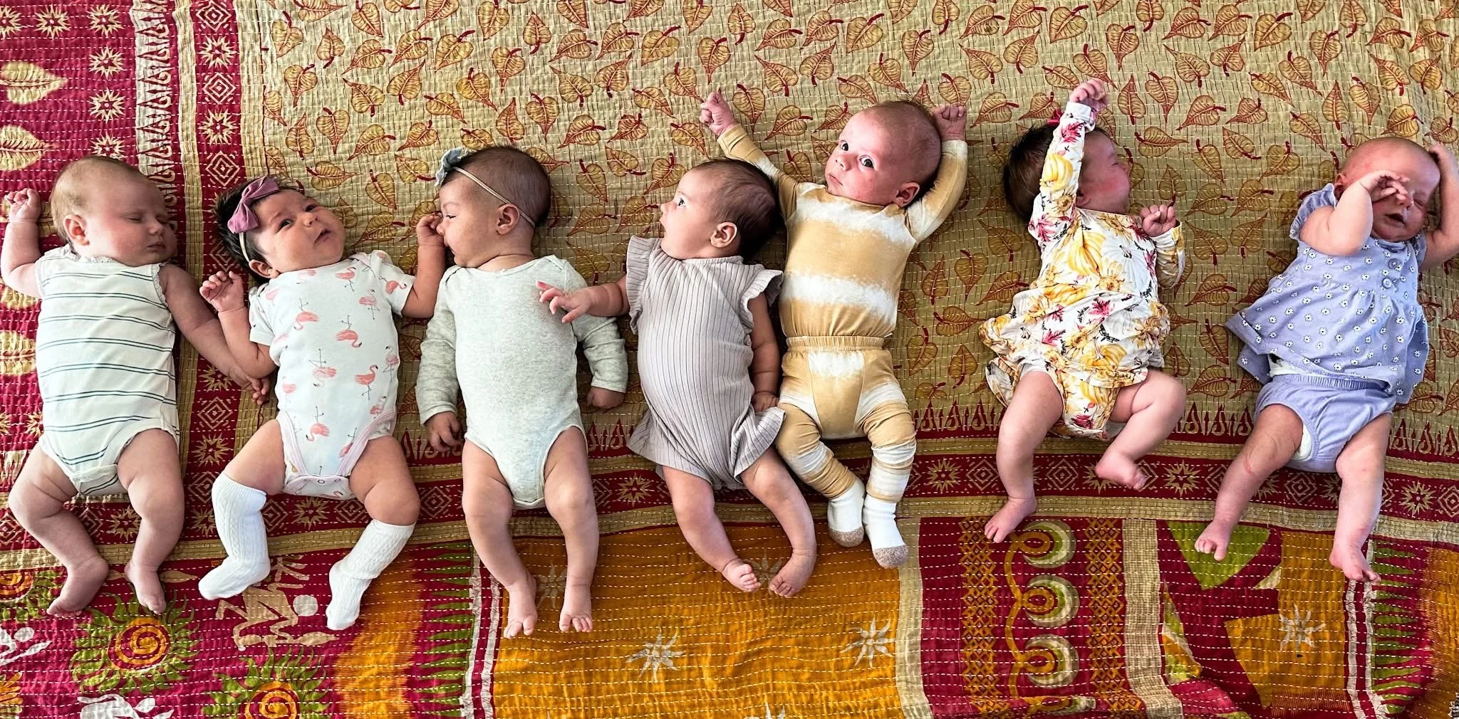 Group of newborn babies lying side by side on a patterned blanket, representing early infant development, newborn care, and supportive lactation and postpartum services