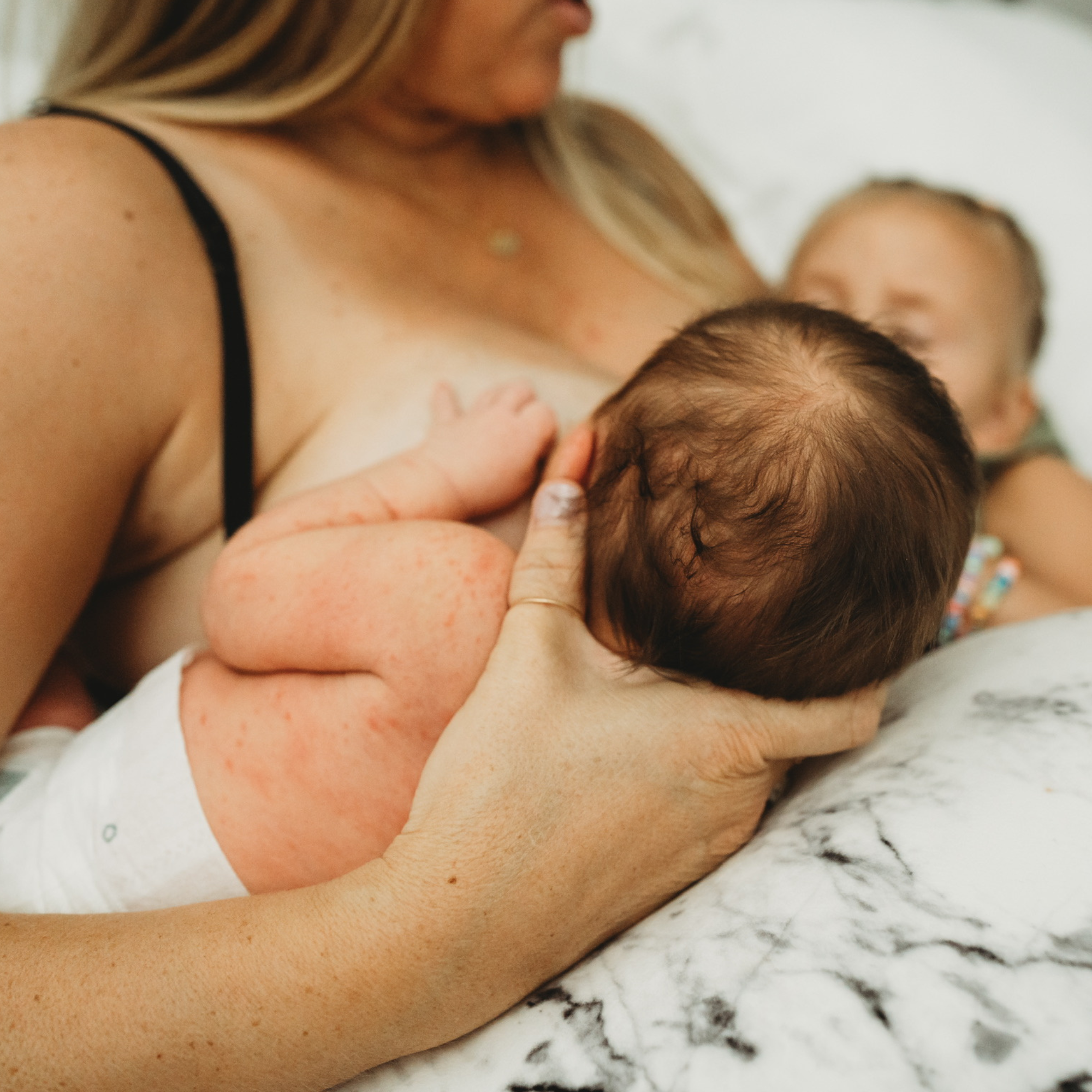 Mother breastfeeding a newborn while cradling the baby’s head, highlighting lactation support, proper latch, and close bonding during infant feeding