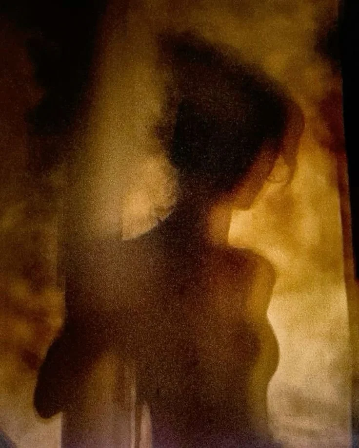 Silhouette of a woman viewed in profile with her head turned slightly downward, dark hair, and a dark top, set against a warm, textured background.