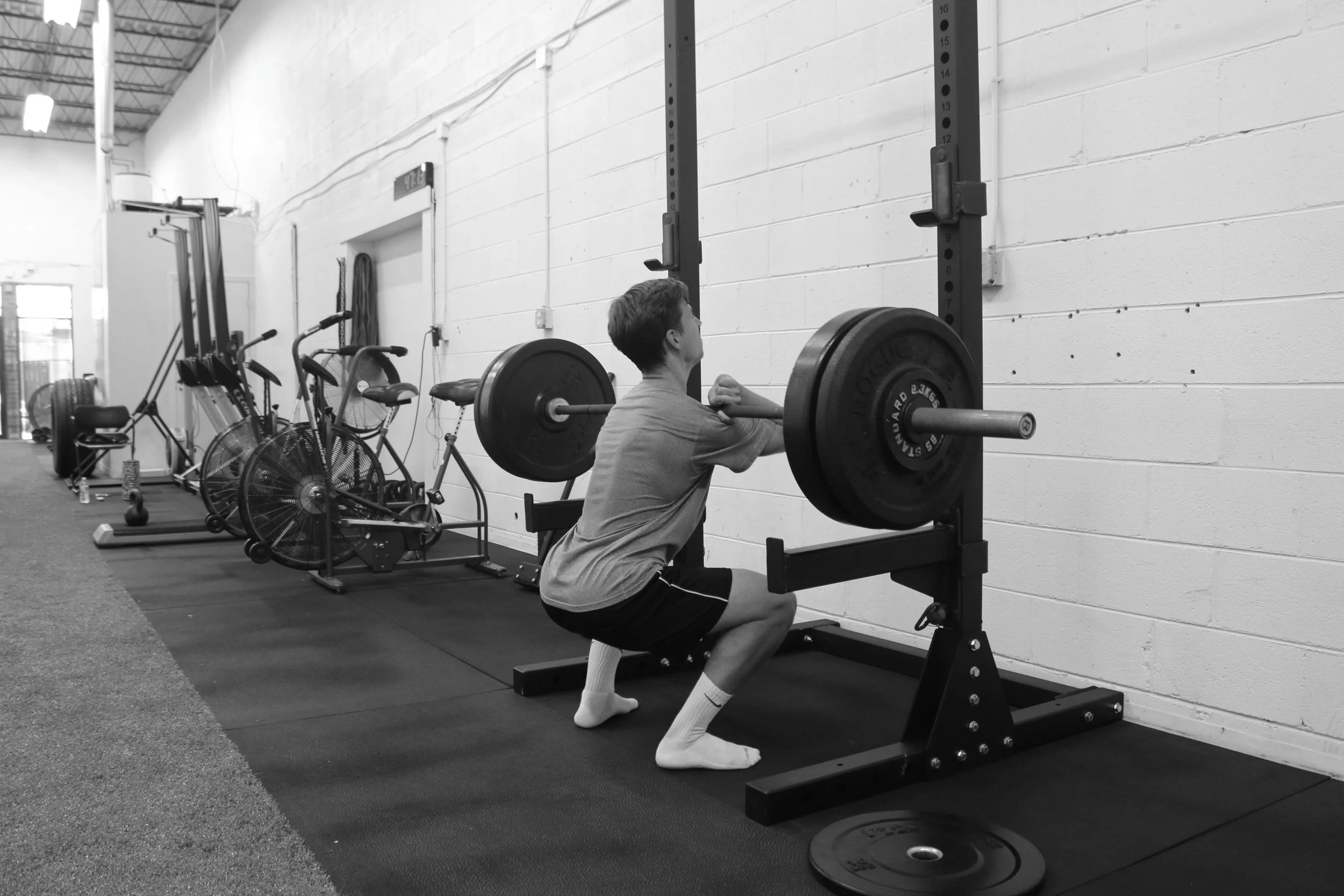 A man squatting with a barbell in a gym, preparing to lift weights.