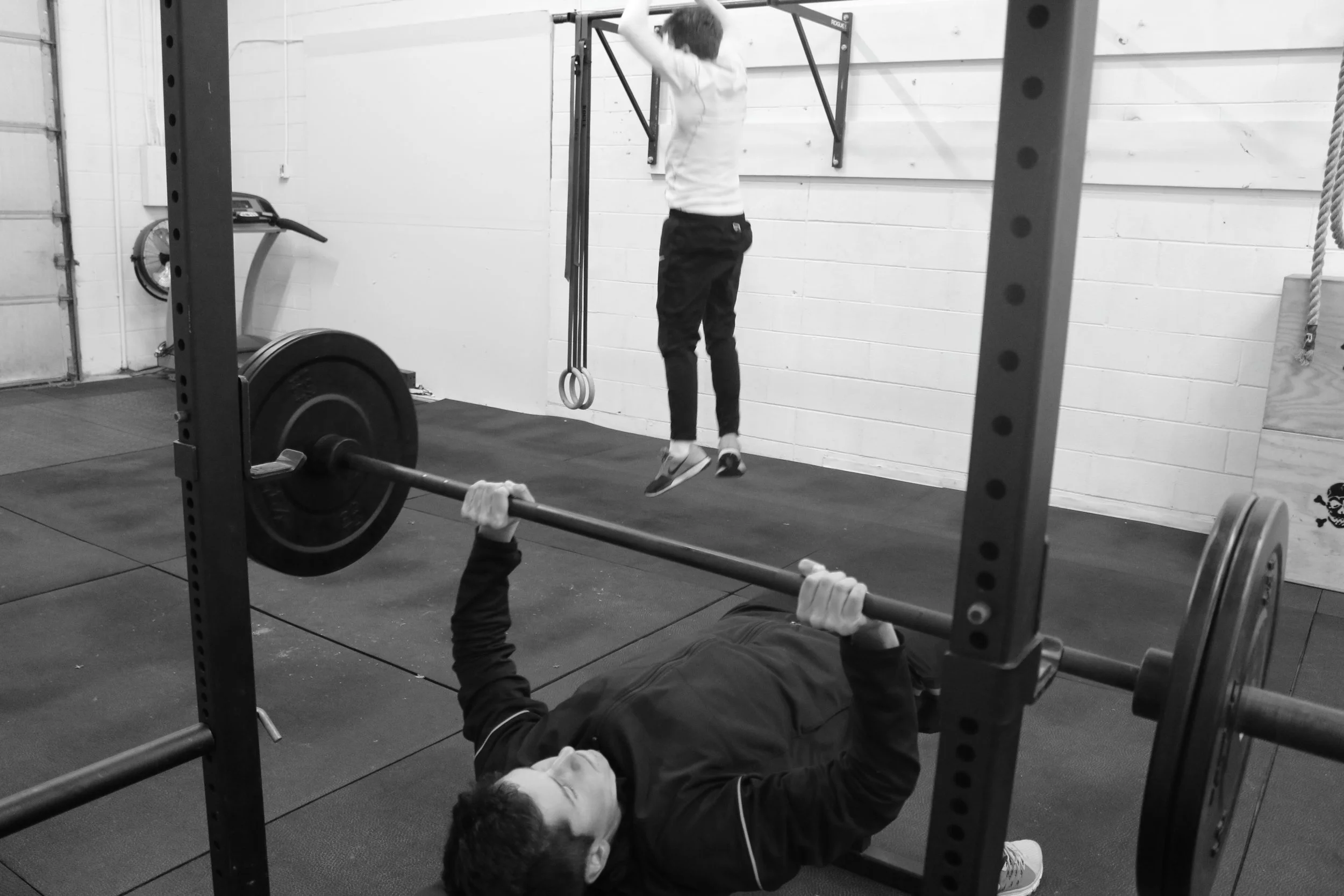 A person lying on the ground lifting a barbell with weights in a gym.