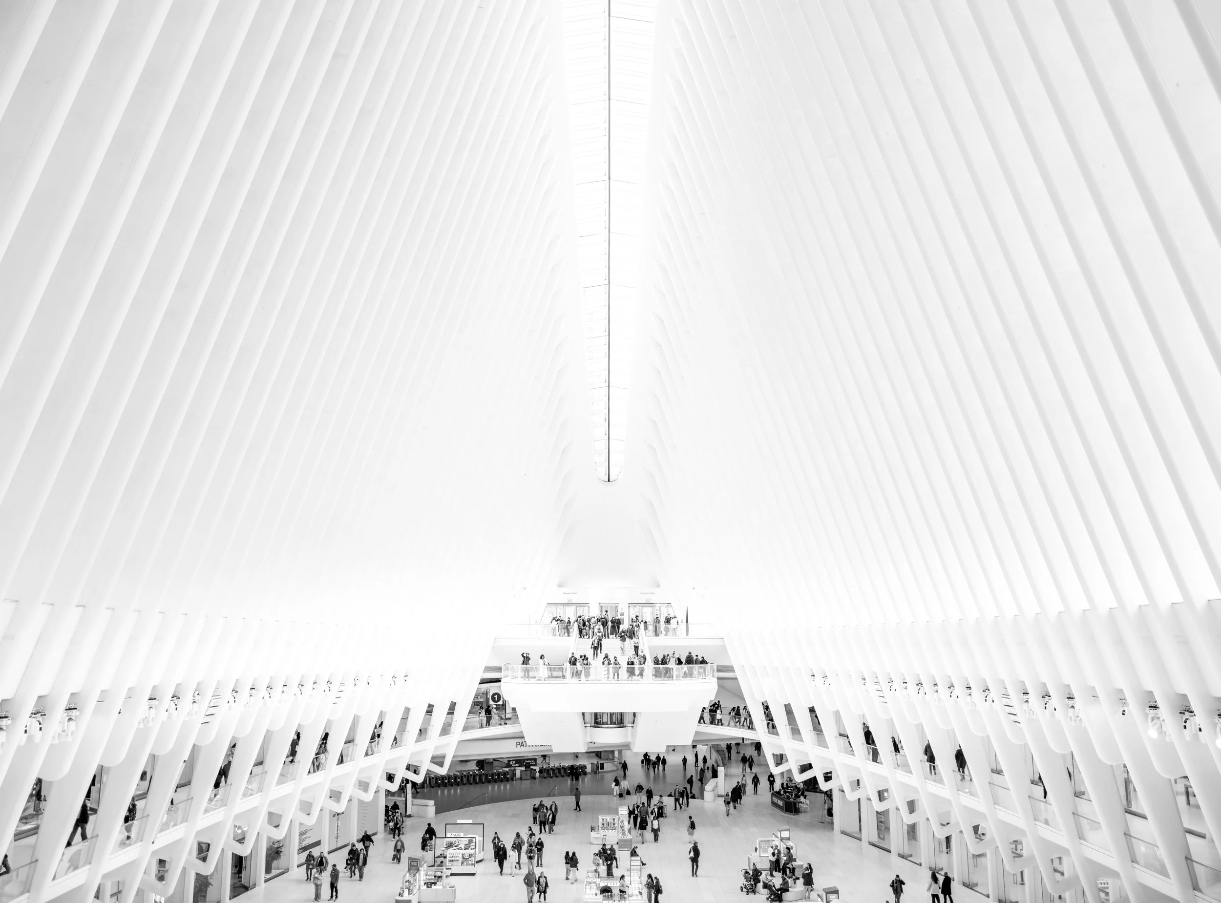 Intérieur d'une station de métro moderne avec une architecture épurée en blanc, plusieurs niveaux et des gens se déplaçant.