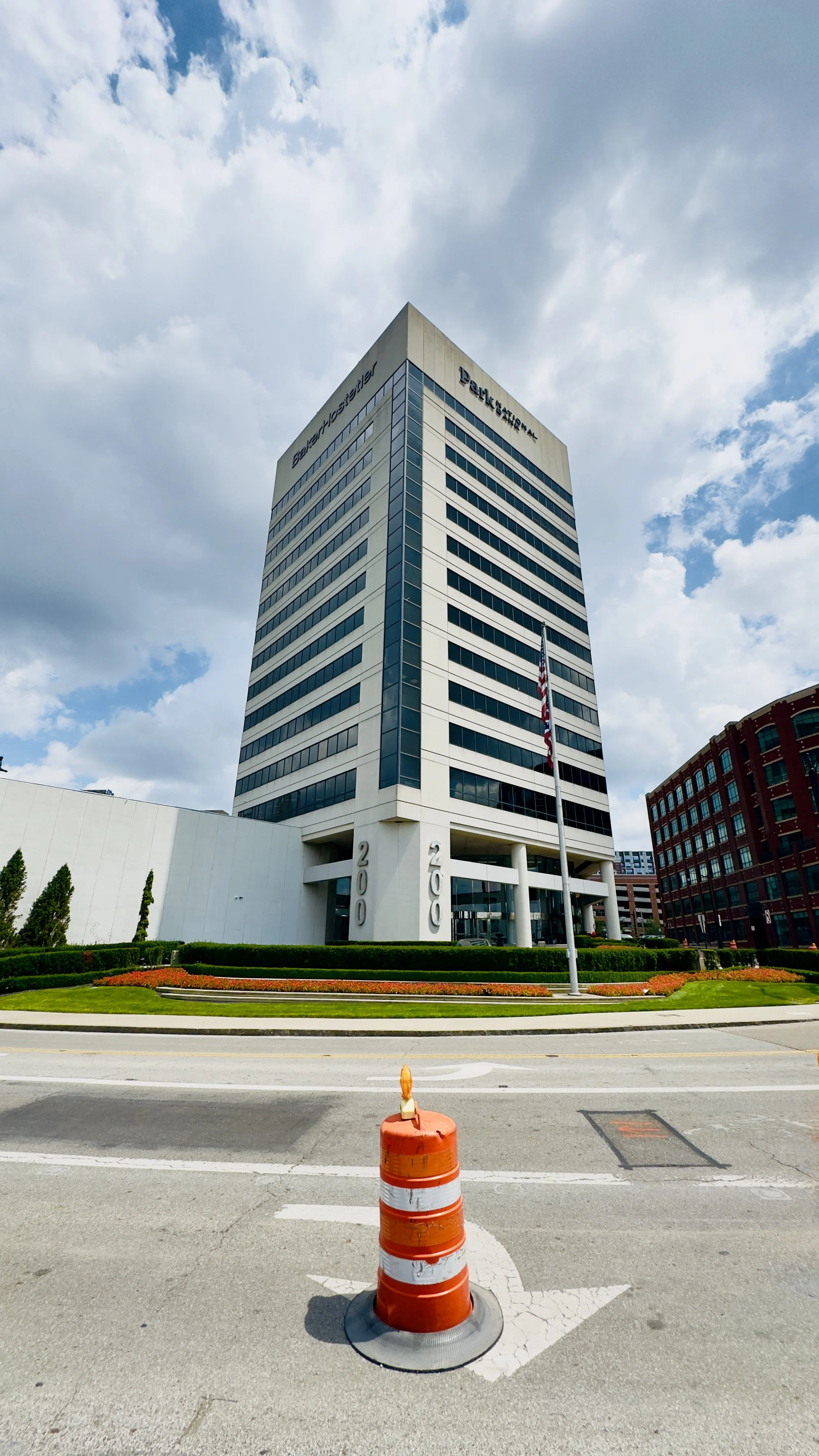 Une grande tour d'affaires avec le logo 'Bahamas Petroleum' en haut, entourée d'un paysage urbain, un feu de signalisation orange et blanc au premier plan, un ciel partiellement nuageux.