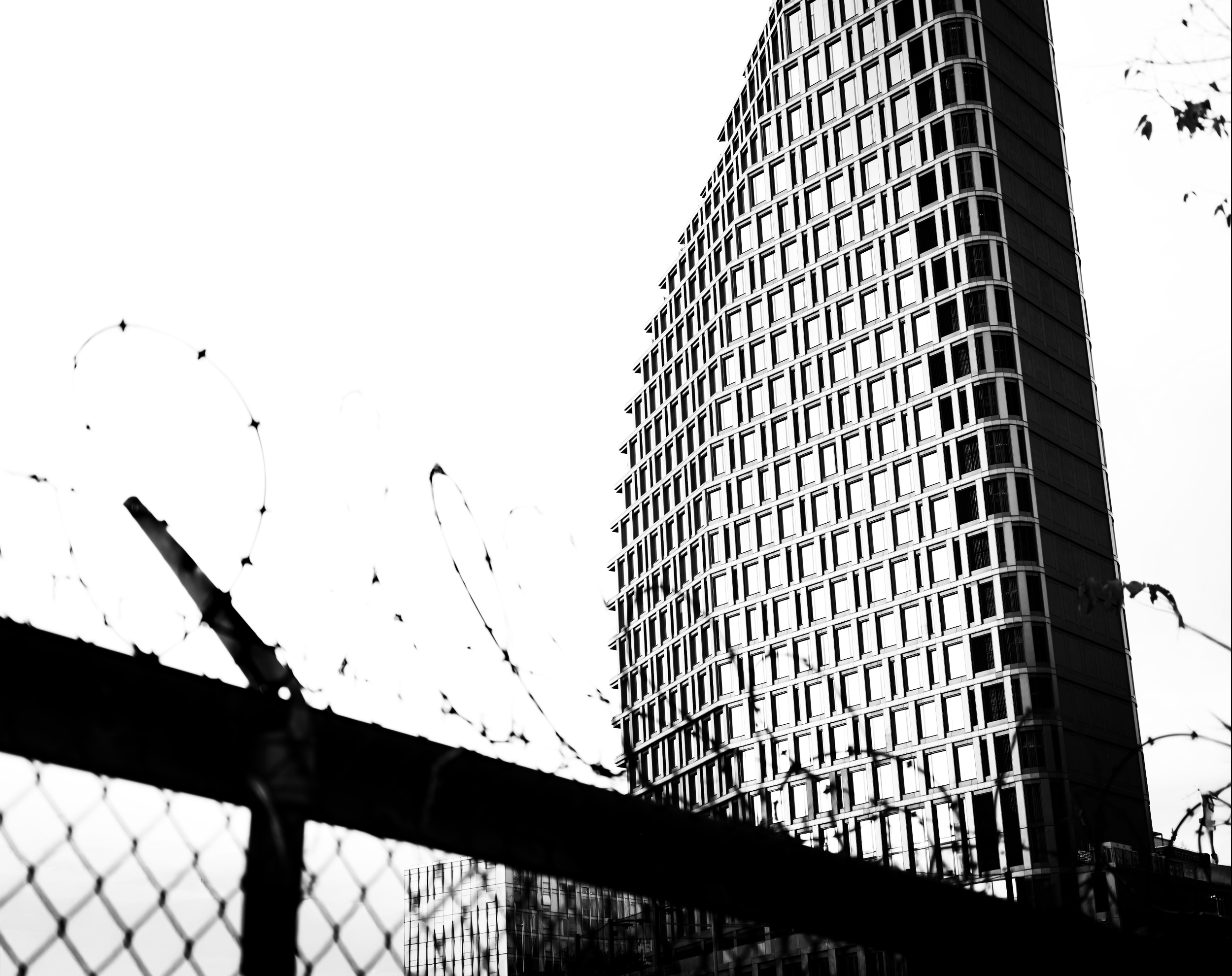 Une grande tour moderne en verre derrière une barrière de fil de fer barbelé.