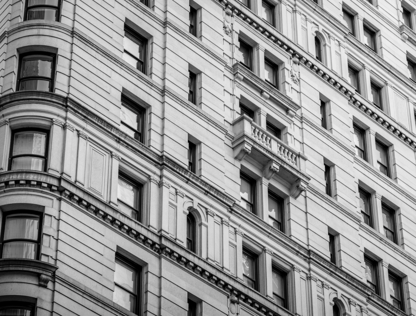 Vue en angle d'un immeuble ancien en pierre avec de nombreuses fenêtres rectangulaires et décorations architecturales classiques.