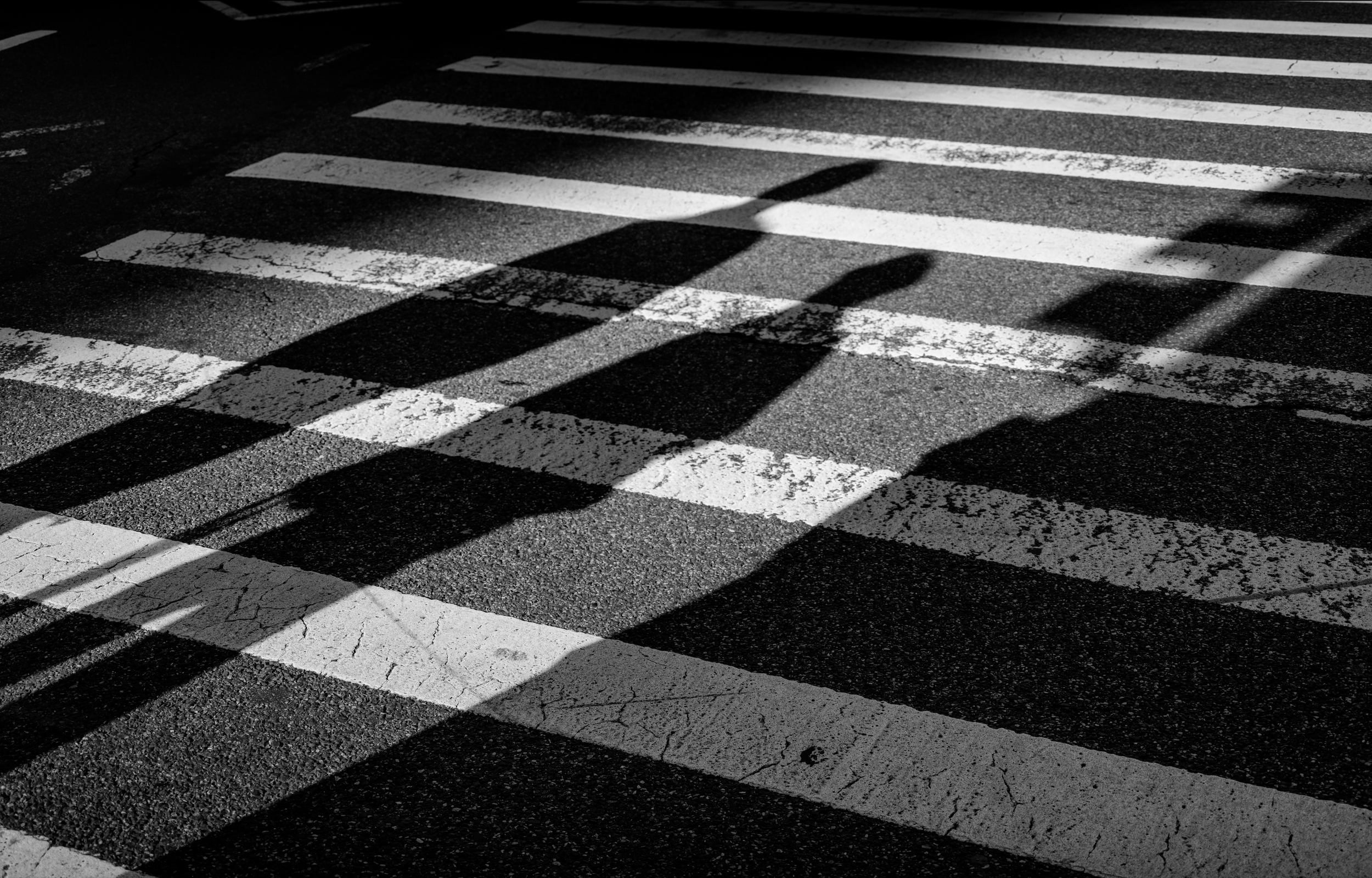 Schéma en noir et blanc d'un passage piéton avec les ombres de lampadaires projetées sur la chaussée.