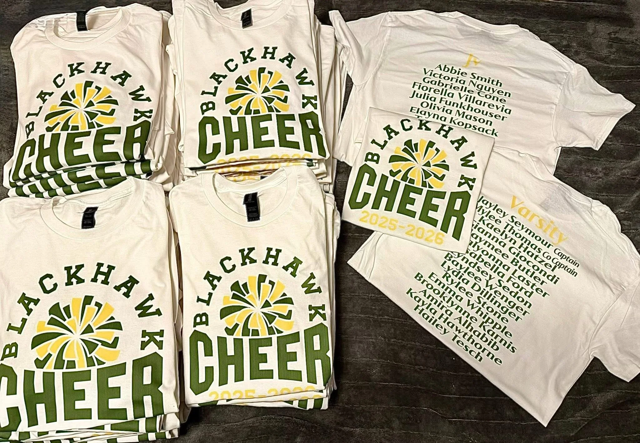 white tshirts with a green and yellow cheer pom pom, arched text above the pom pom in green that says blackhawk then the word cheer in green under the pom pom