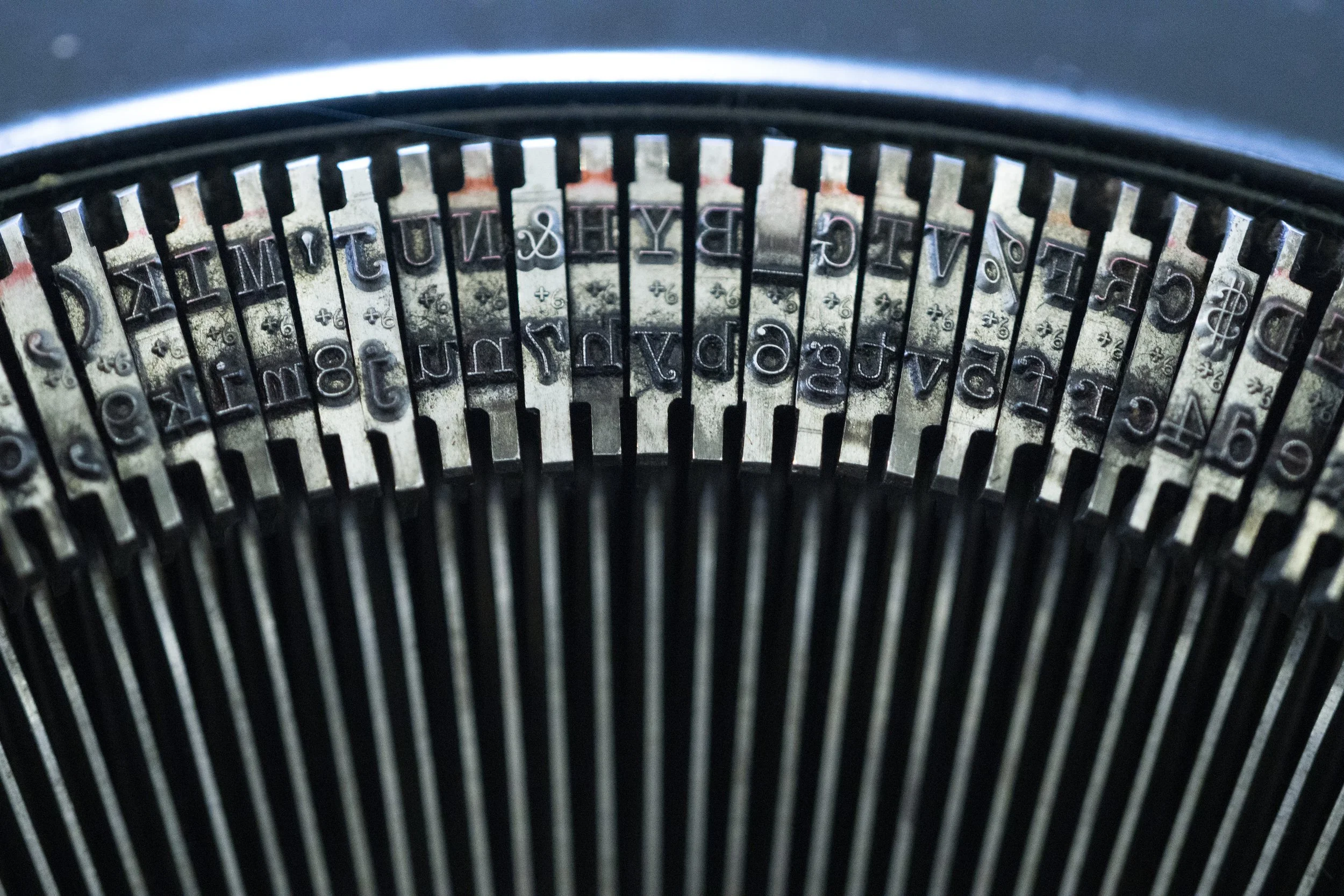 Close-up of the metal typebars inside a vintage typewriter, showing uppercase and lowercase letters and symbols.