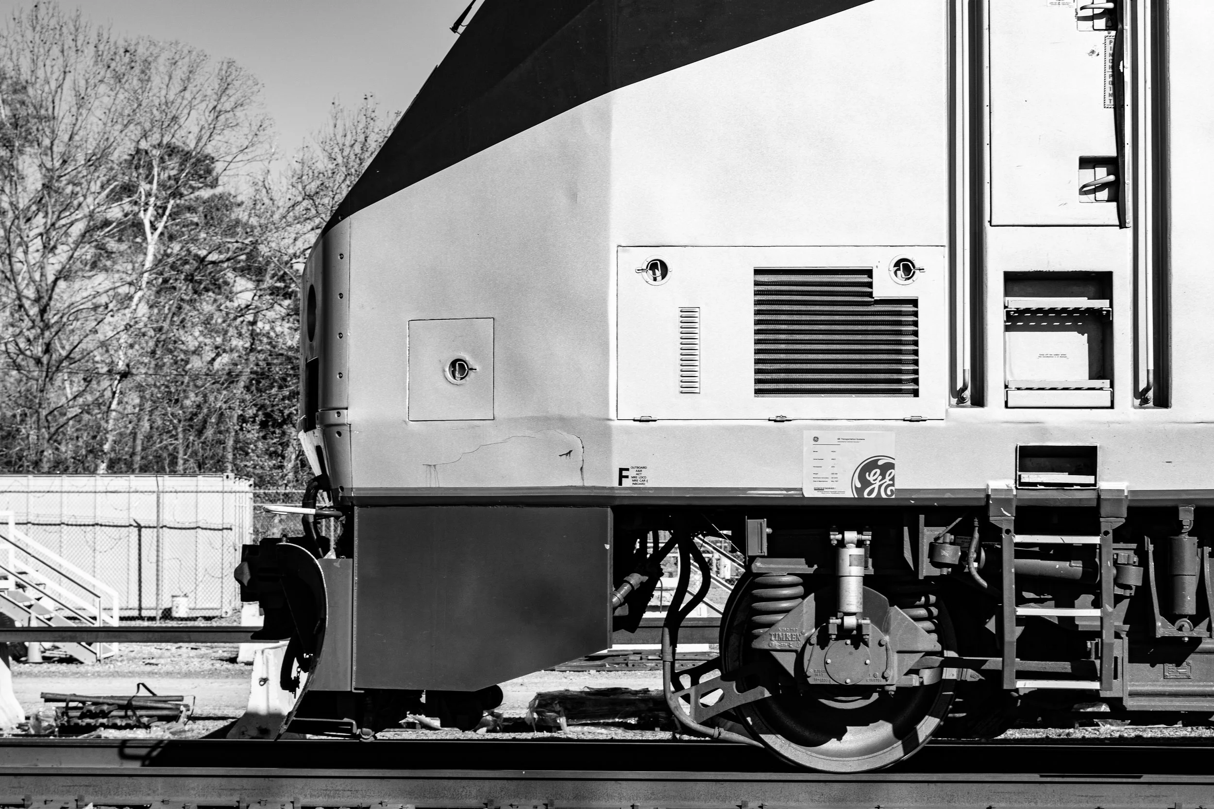 Close-up of the side of a train car showing wheels, mechanical parts, and access panels in black and white.
