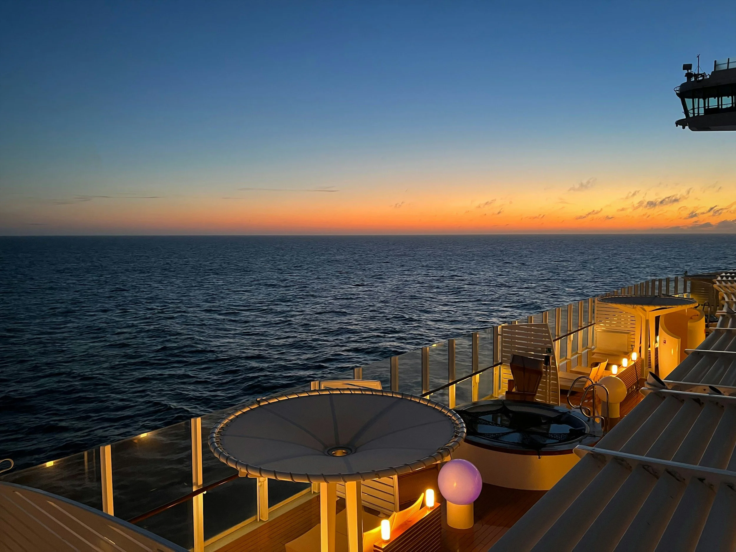 Vista del mare al tramonto da una nave, con luci soffuse sull'area esterna e un cielo colorato dal tramonto.