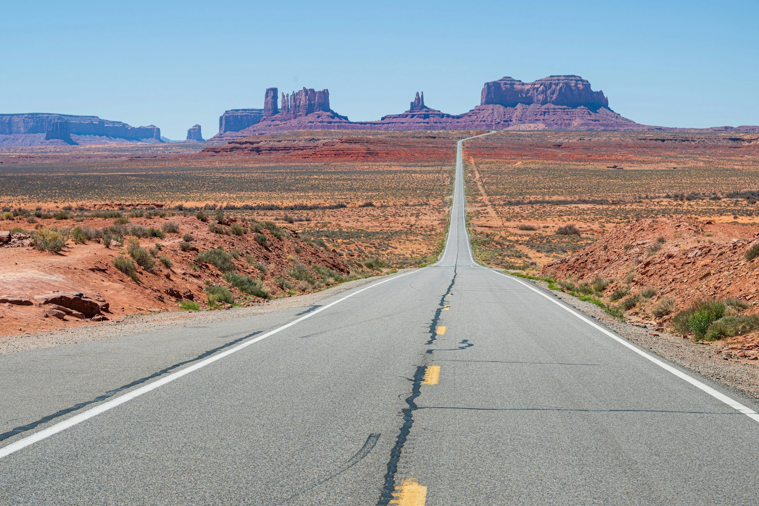 Strada asfaltata nel deserto con rocce rosse e formazioni rocciose au lontano.
