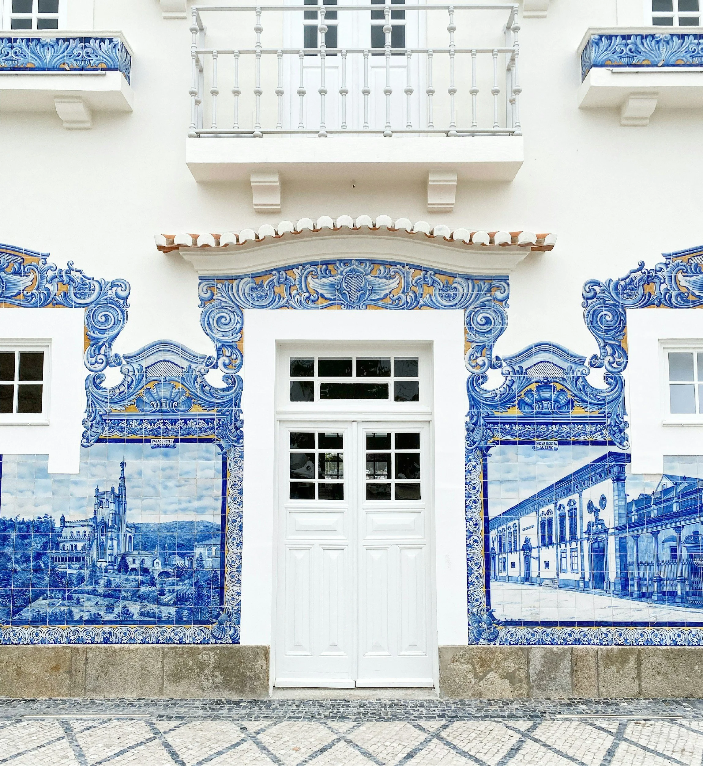 Facciata di un edificio decorata con piastrelle di azulejos blu e bianche, raffiguranti paesaggi e architetture.