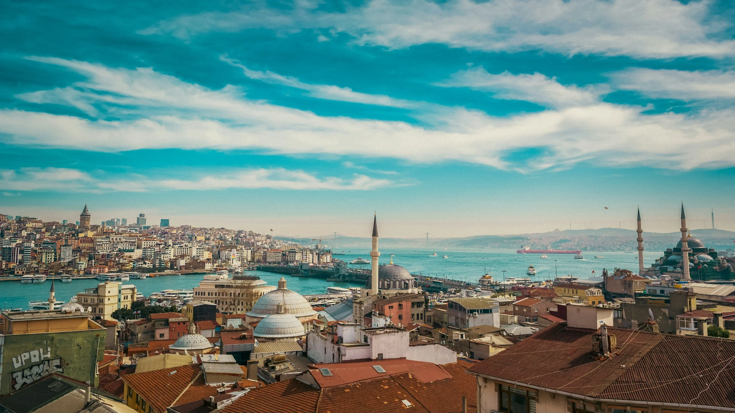 Vista panoramica di Istanbul, Turchia, con le sue case, moschee con minareti, il Bosforo con barche e navi, e il ponte sullo sfondo sotto un cielo azzurro con nuvole