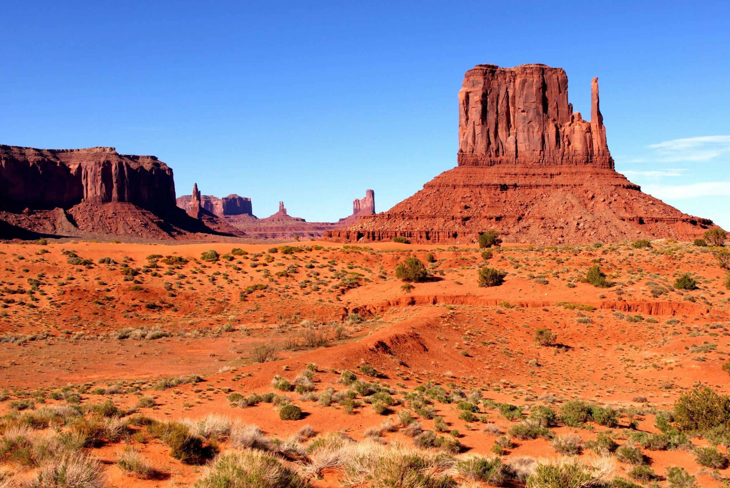 Paesaggio desertico con grandi formazioni rocciose rosse sotto un cielo blu chiaro.