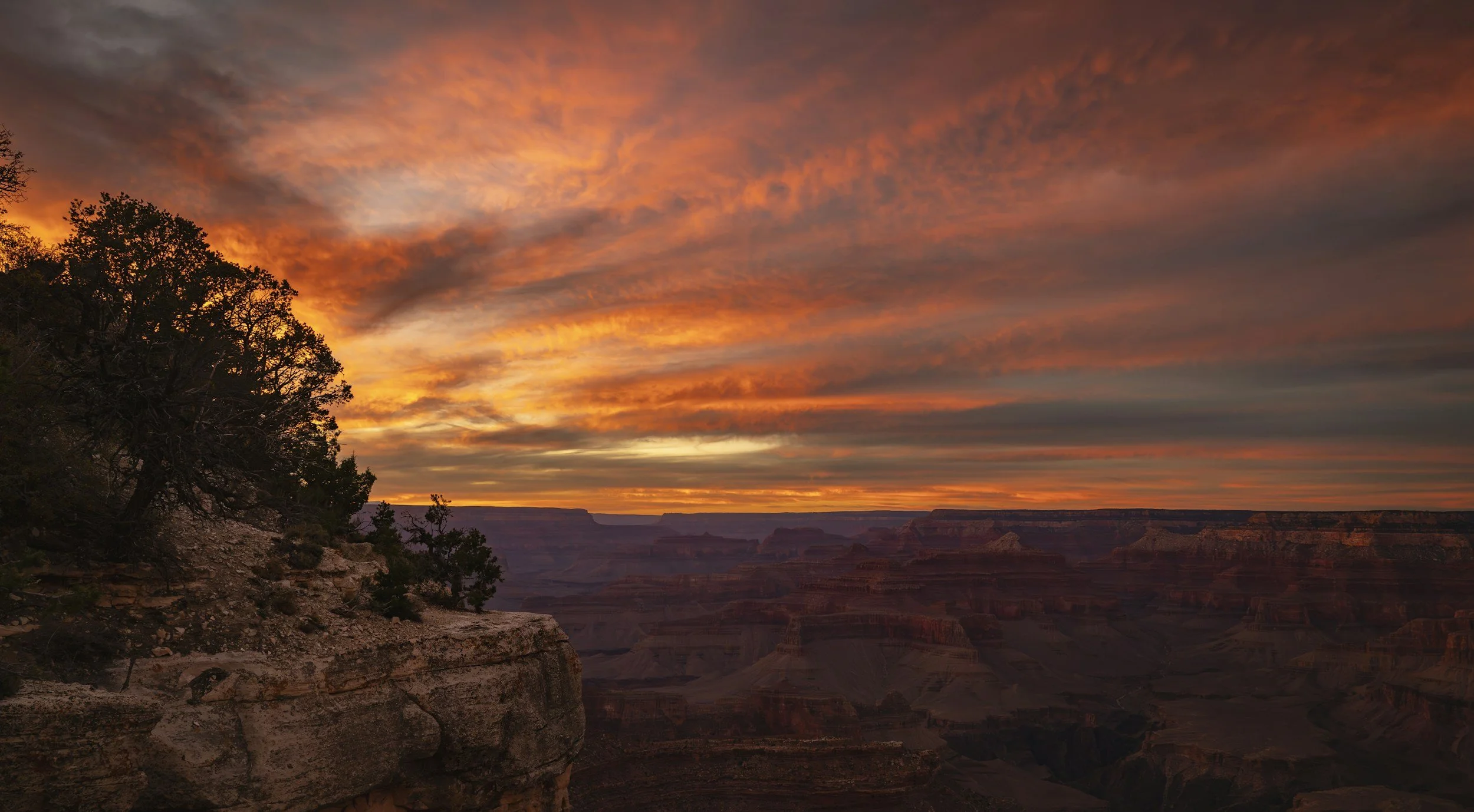 Un tramonto sopra il Grand Canyon con nuvole colorate di arancione e rosa nel cielo e le pareti del canyon in lontananza.