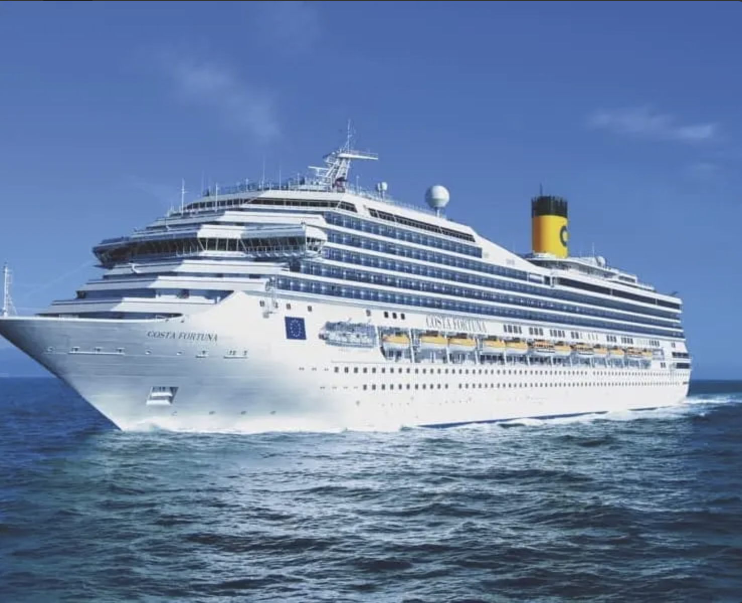 Una nave da crociera bianca in mare con il logo Costa Crociere sulla fiancata, una grande ciminiera gialla e una rete di balconi.