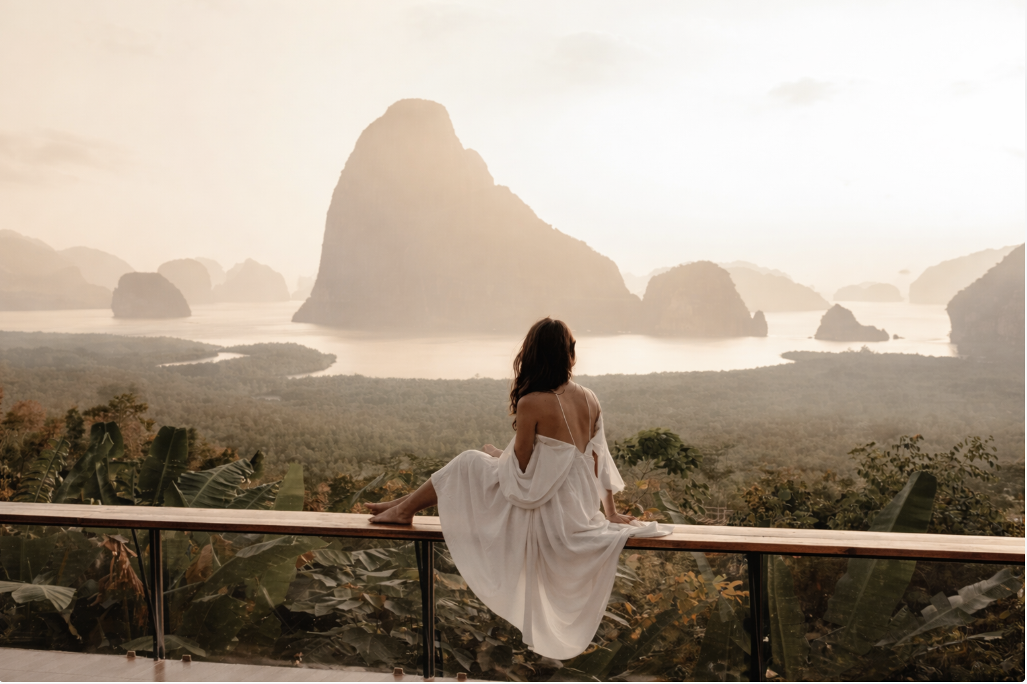 donna seduta, abito chiaro, panorama ampio con isole rocciose e luce morbida