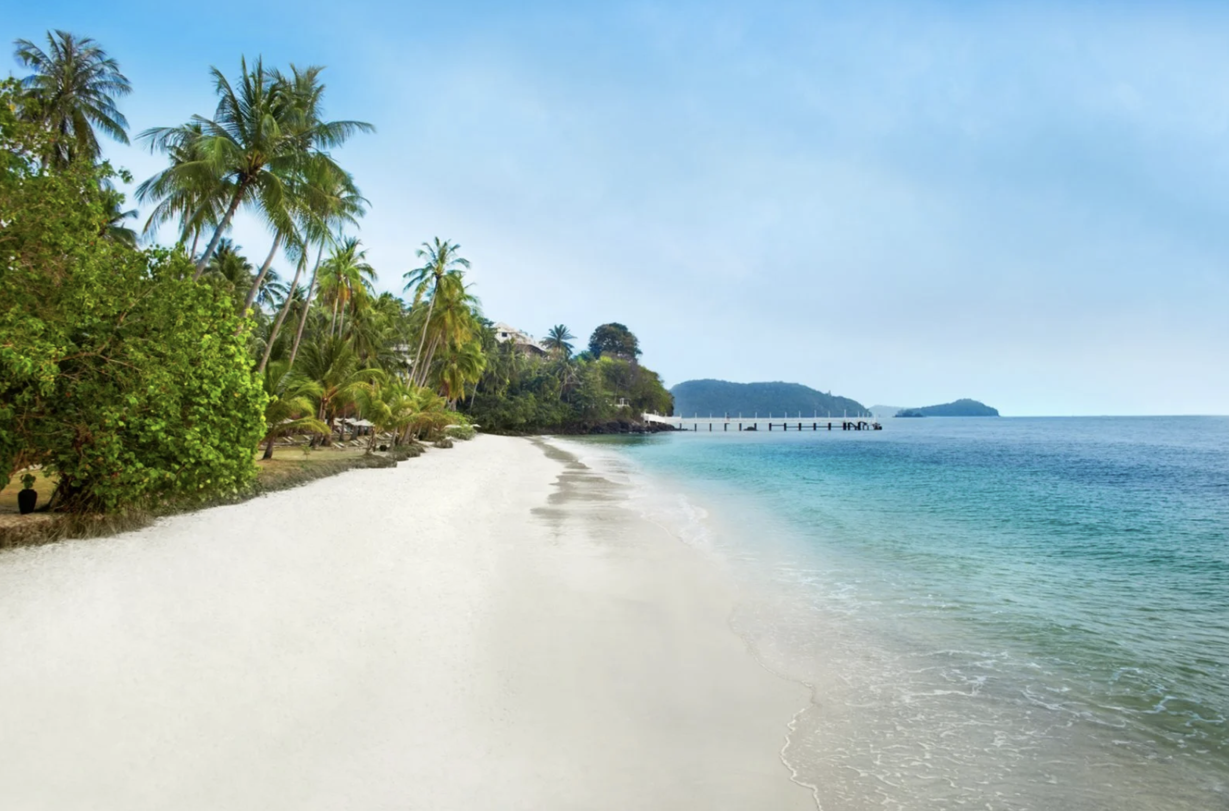 Spiaggia tropicale con sabbia bianca, alberi di palme e mare azzurro sotto un cielo sereno.