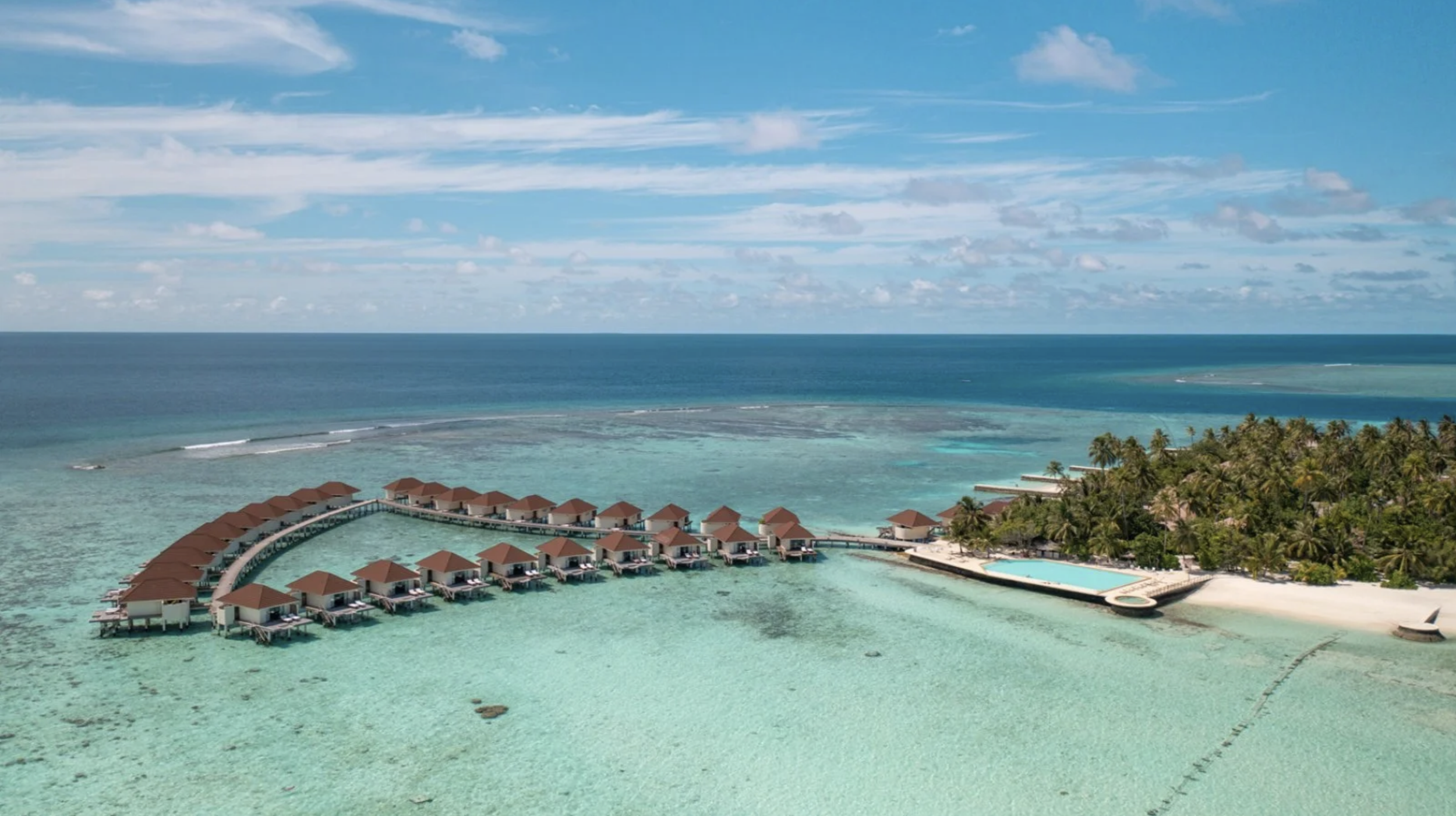 Vista aerea di bungalow situati su una barriera corallina con acqua cristallina e una spiaggia piena di palme