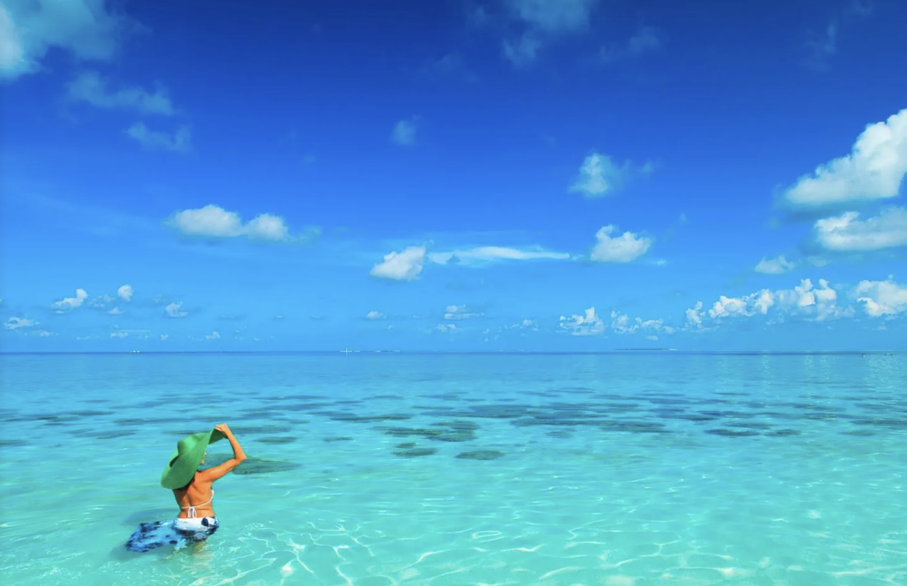 Donna con cappello verde che si trova nell'acqua vicino alla spiaggia con cielo azzurro e nuvole