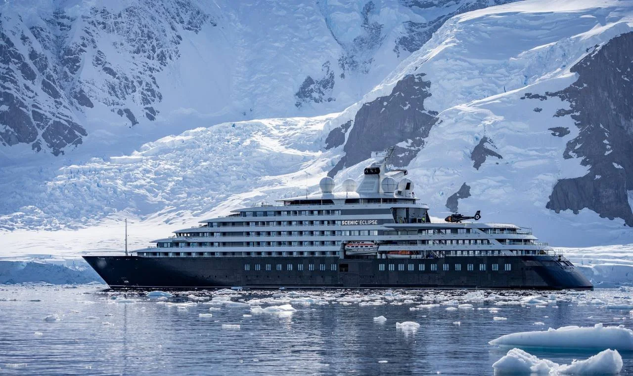 A large cruise ship named Scenic Eclipse sailing through icy waters with snow-covered mountains in the background.