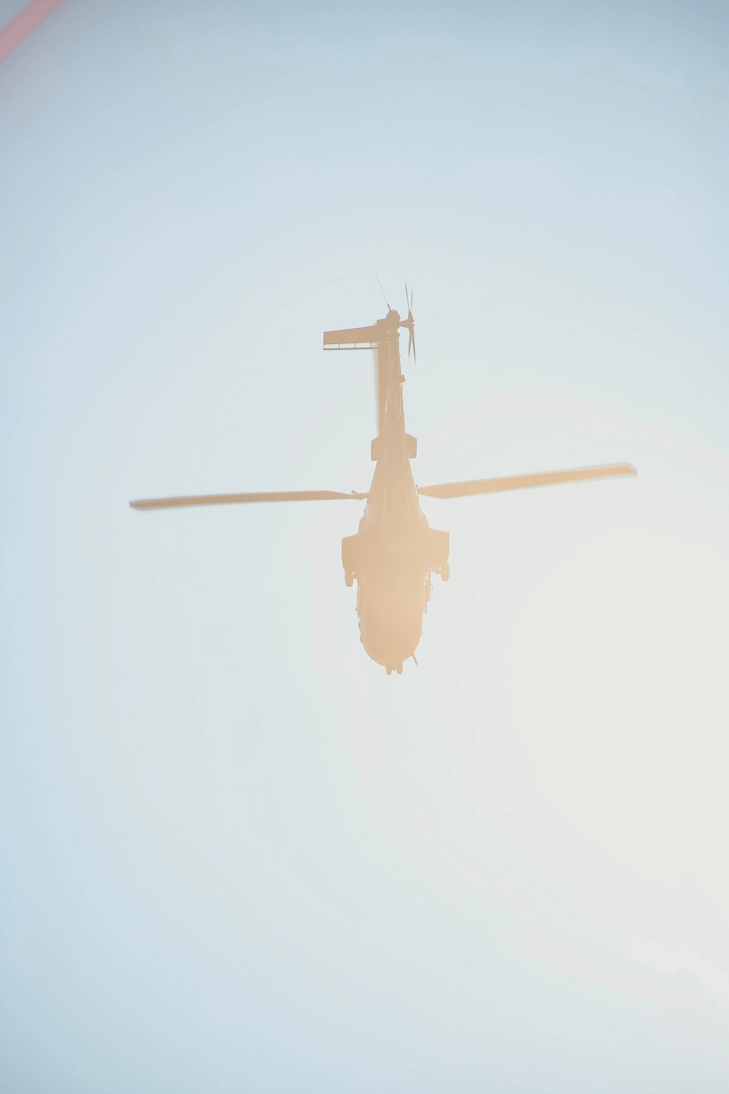 Silhouette of a helicopter in flight against a bright sky, captured from below.