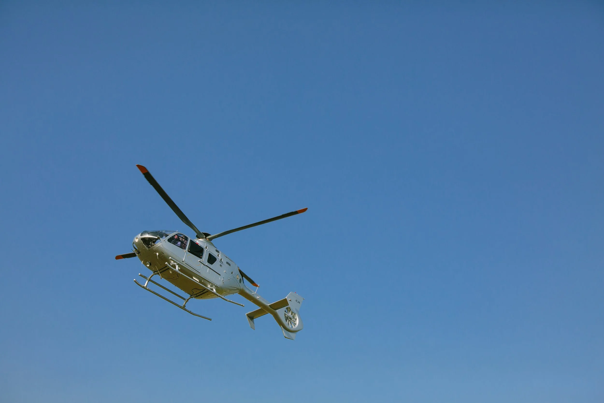 A white helicopter flying in a clear blue sky.