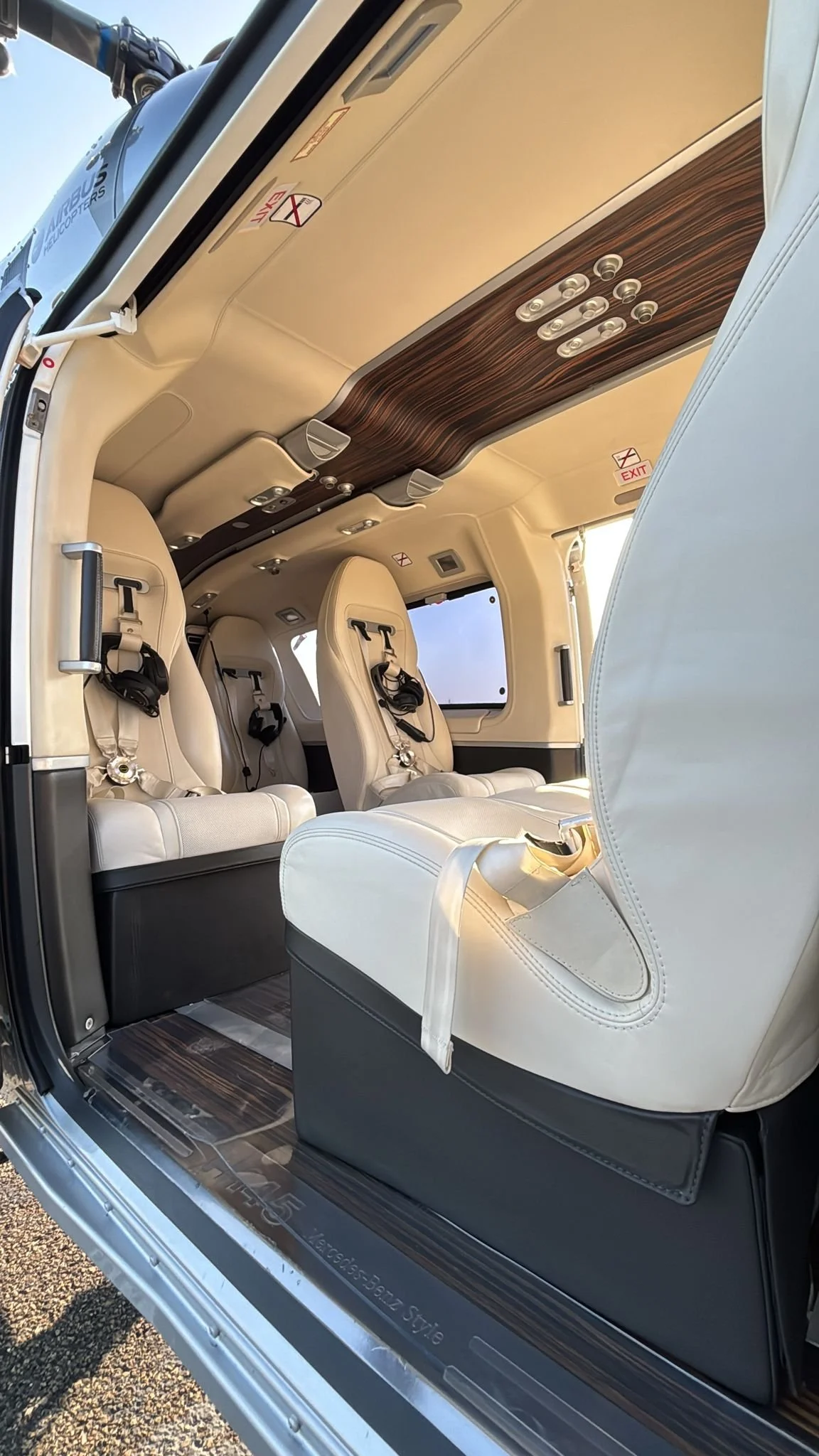 Interior of a helicopter with white leather seats, a wooden ceiling, and multiple control buttons overhead.