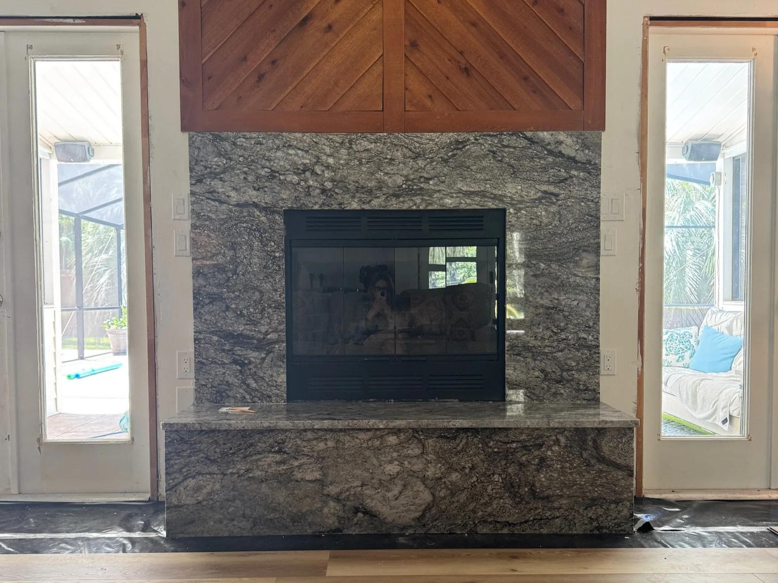 A modern fireplace with a granite surround and wooden accent above, flanked by two glass doors leading to outdoor areas with patio and furniture.