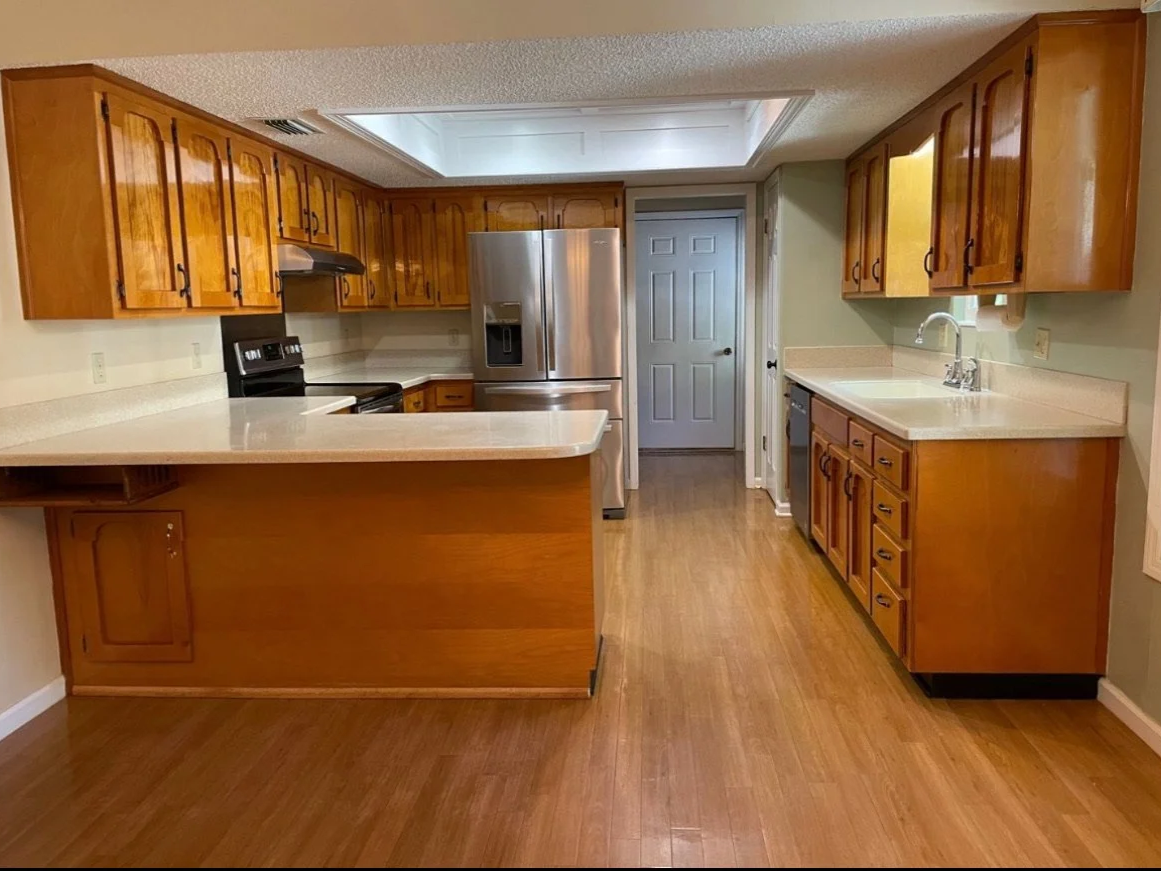 Kitchen with wooden cabinets, white countertops, stainless steel refrigerator, black stove, kitchen sink, and hardwood floors.
