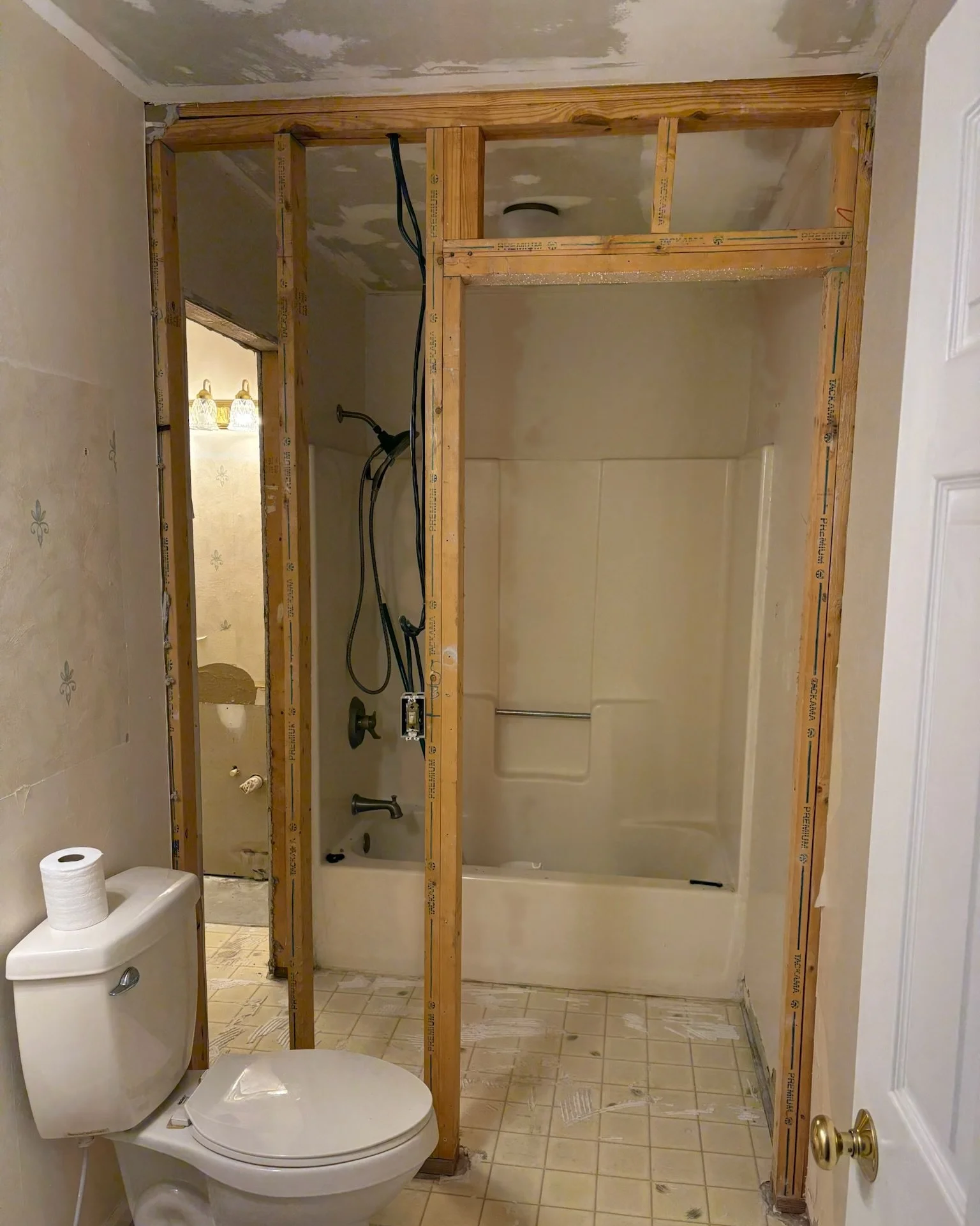 Bathroom undergoing renovation with exposed wooden framing for a shower or bathtub area, a toilet with toilet paper, and visible electrical wiring.