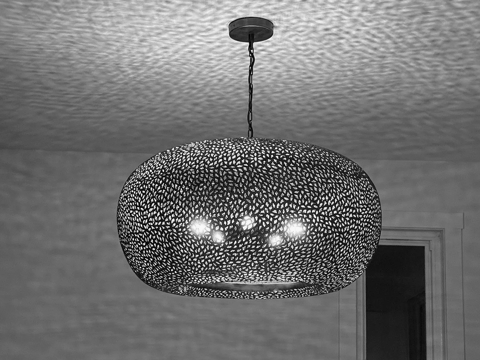 A modern decorative ceiling light fixture with a perforated metal shade hanging from the ceiling.