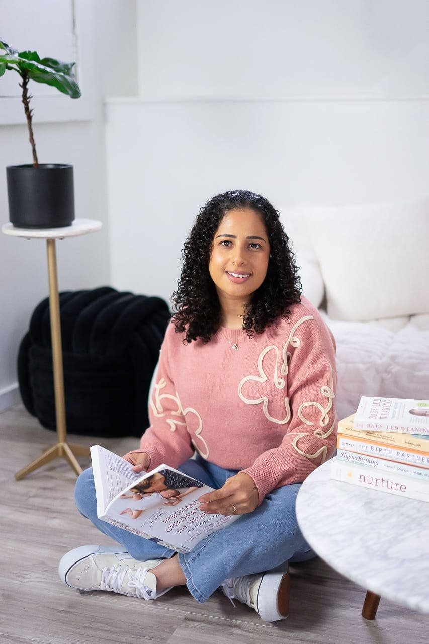 Woman sitting on the floor, reading a magazine in a cozy, well-lit room with a small round table and books.
