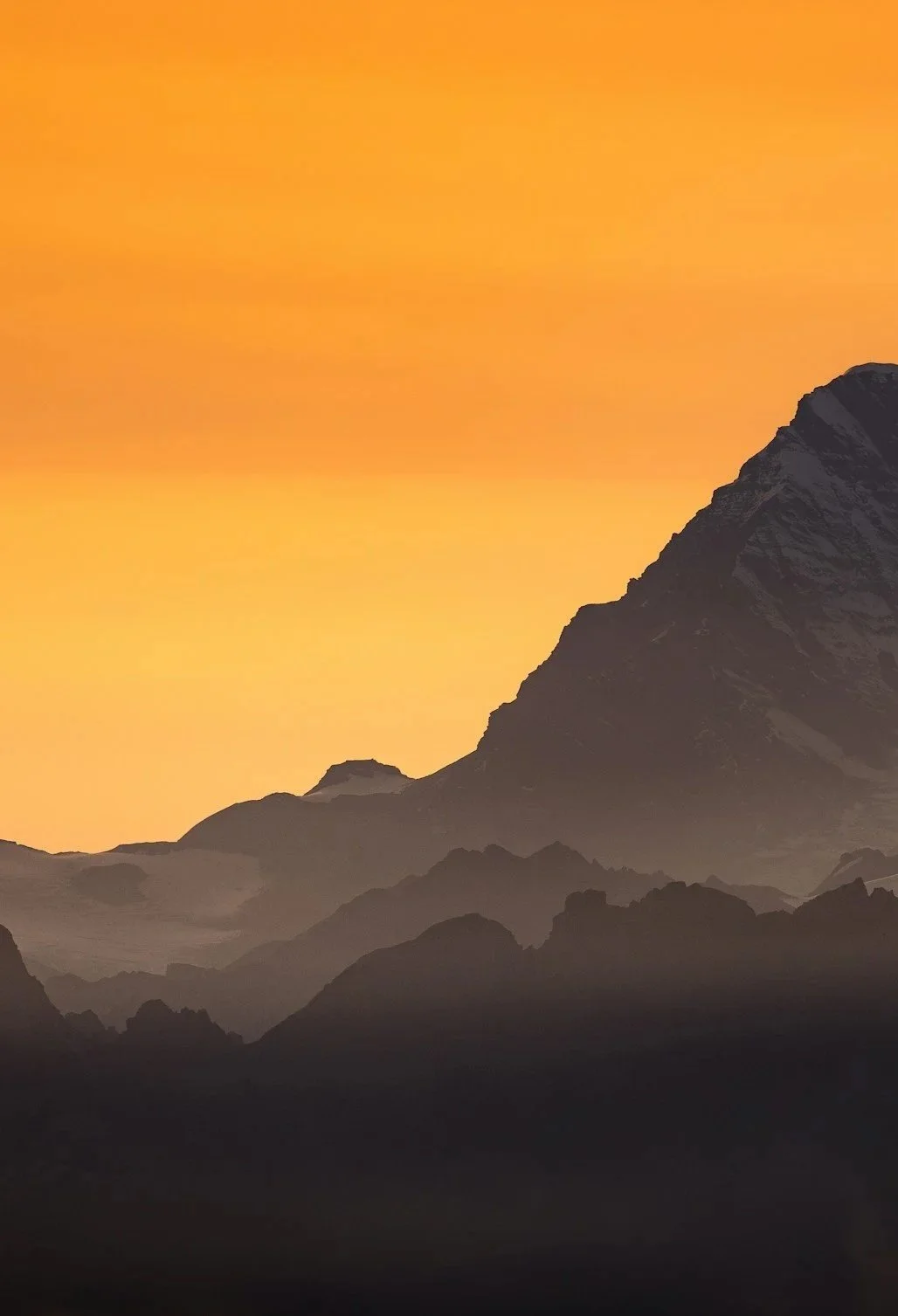 Mountain landscape at sunset with dark mountain silhouettes against an orange sky.