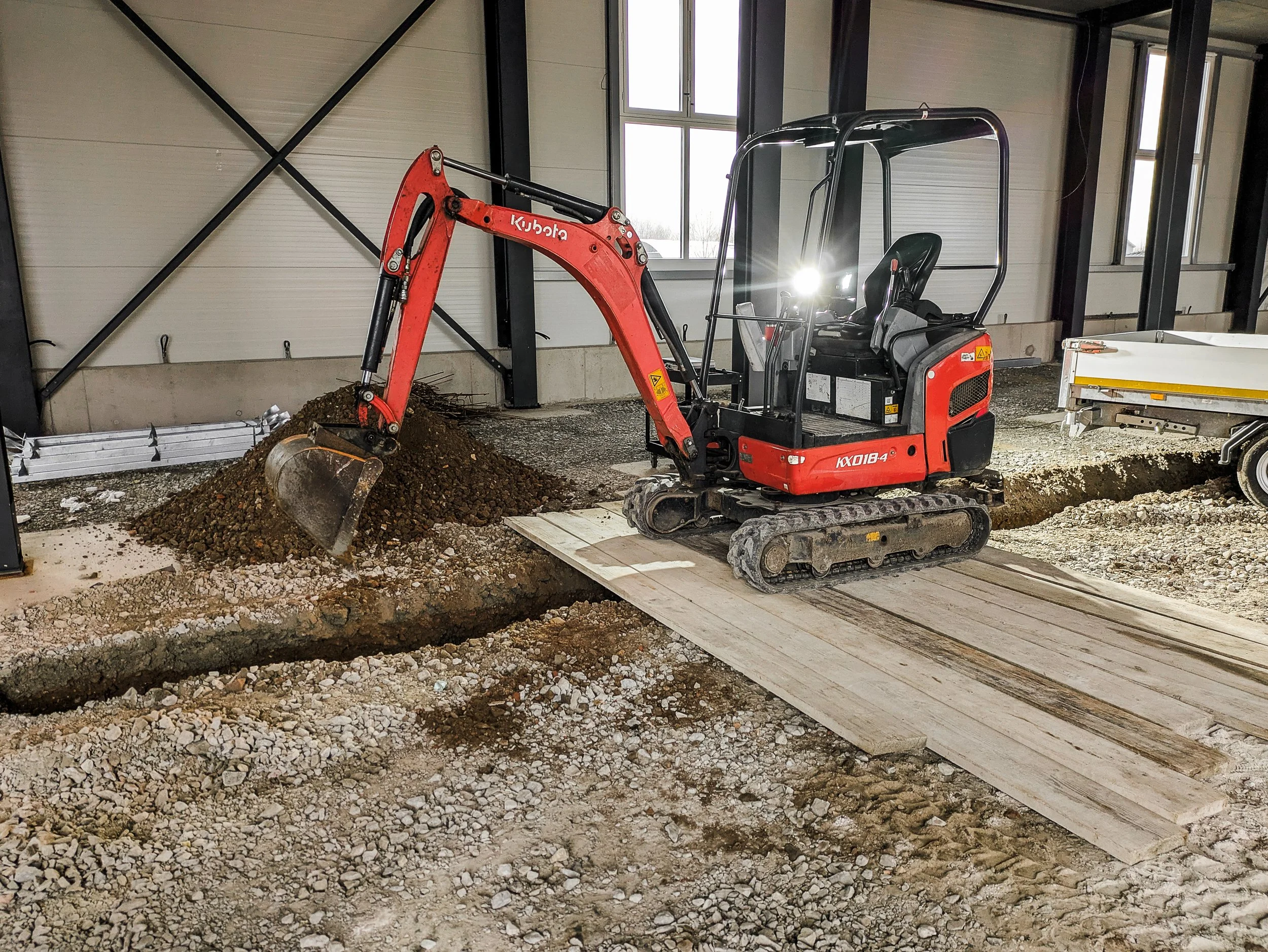 Kleine Bagger mit Schaufel auf einer Baustelle, Erde wird bewegt, im Hintergrund helle Wände und Fenster, Innenraum eines Gebäudes im Bau.