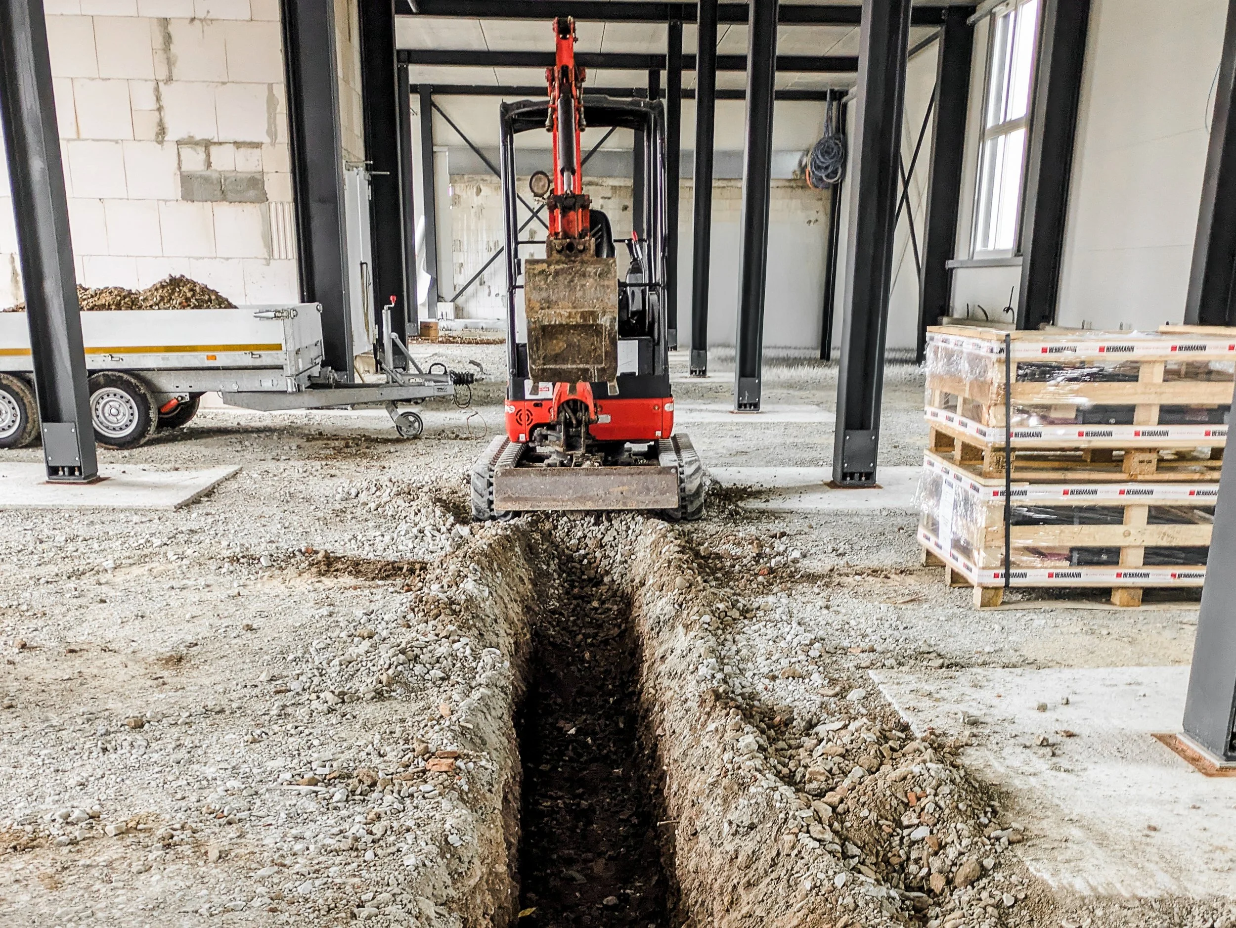 Bauarbeiter auf einer Baustelle beim Graben, ein kleiner Tunnel ist im Boden sichtbar, im Hintergrund Baumaterial und Bauschutt.