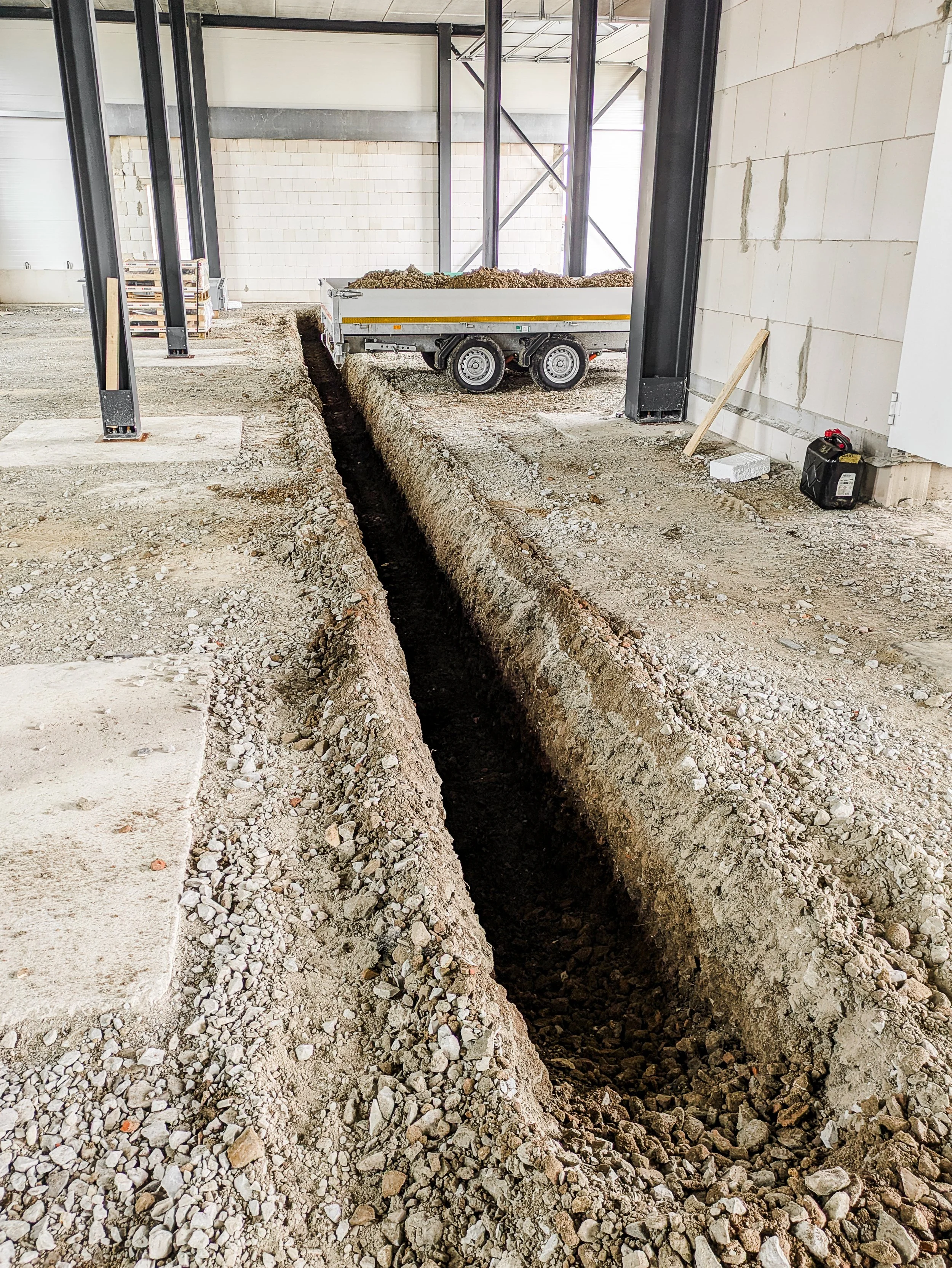 Innenansicht eines Baugebiets mit Graben für Fundamente, Baustruktur aus Stahl und teilweise fertiggestellte Wände.