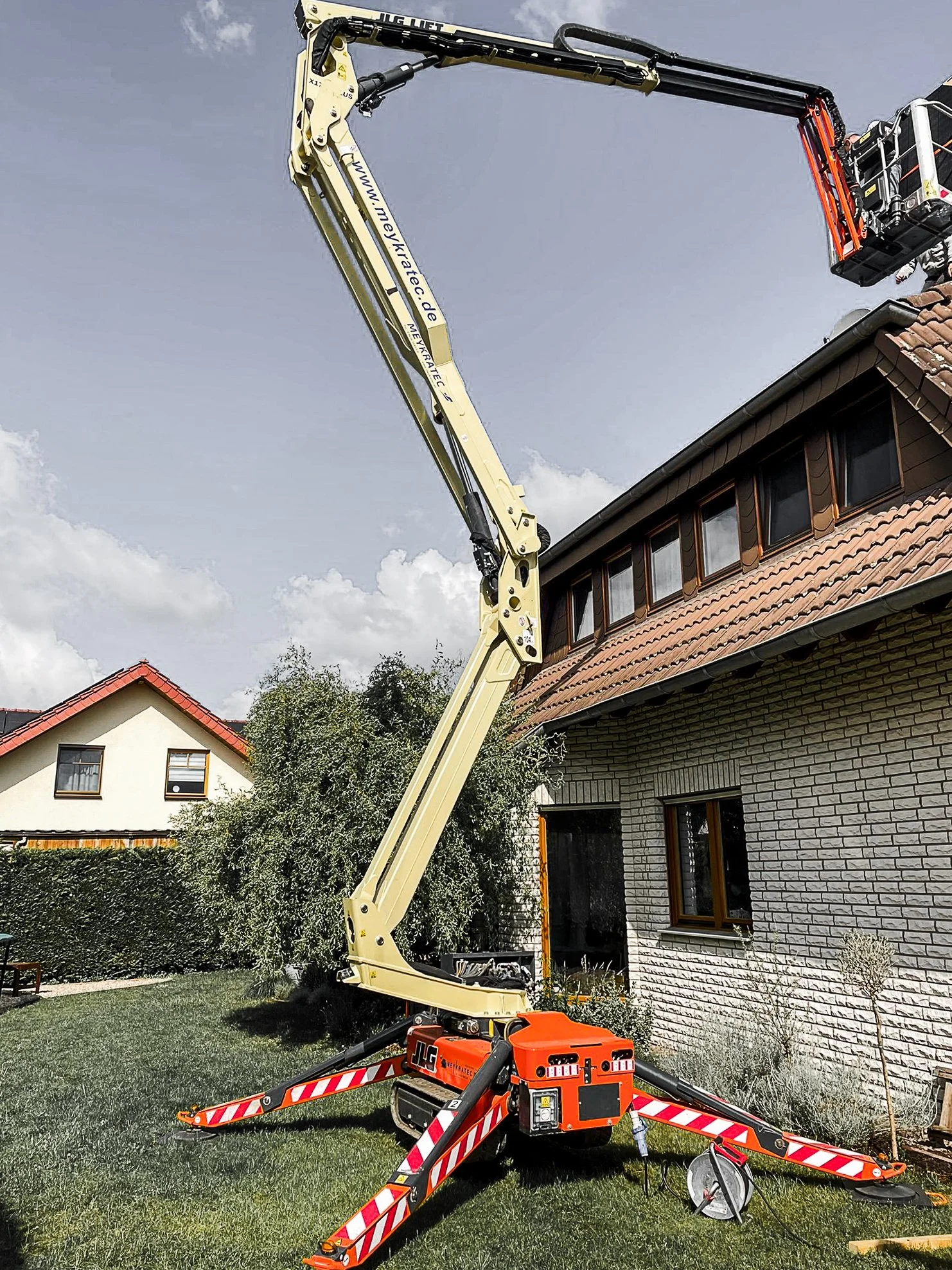 Ein Kran, der an einem Haus im Garten arbeitet, mit einem Dach im Hintergrund, bei schönem Wetter