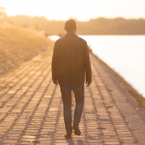 A person walking on a brick pathway beside a river during sunset.