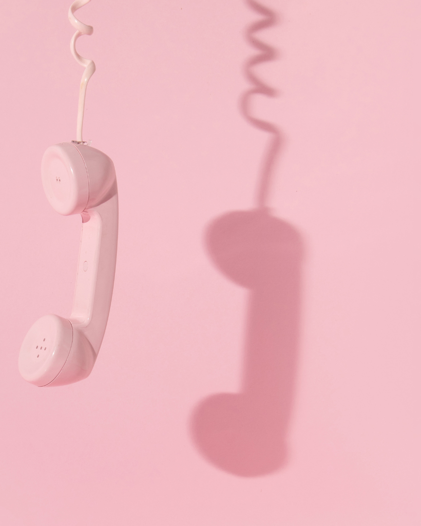 Pink vintage rotary telephone casting its shadow on a pink background.