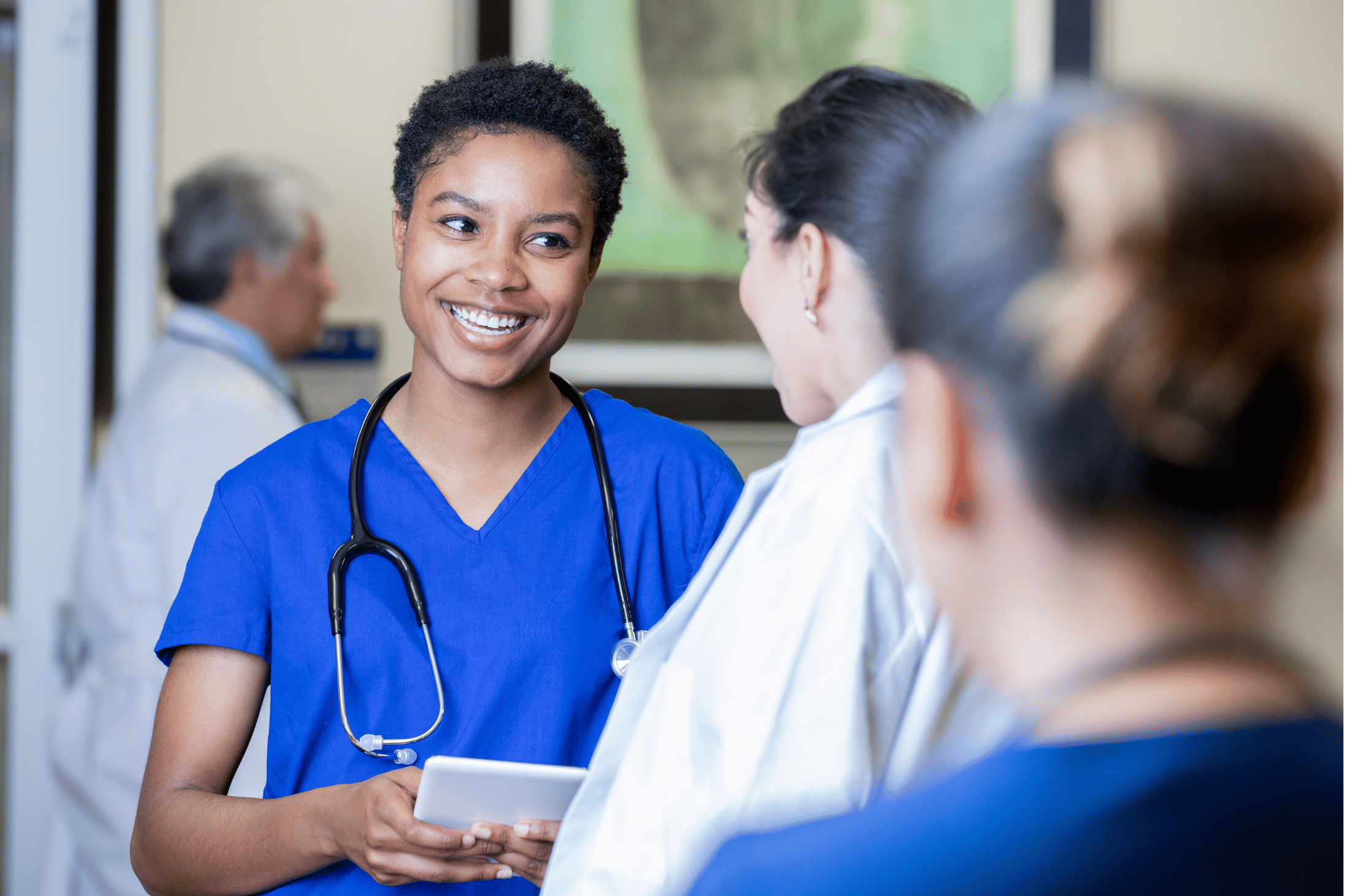 A doctor in blue scrubs with a stethoscope around her neck smiling in conversation with a patient