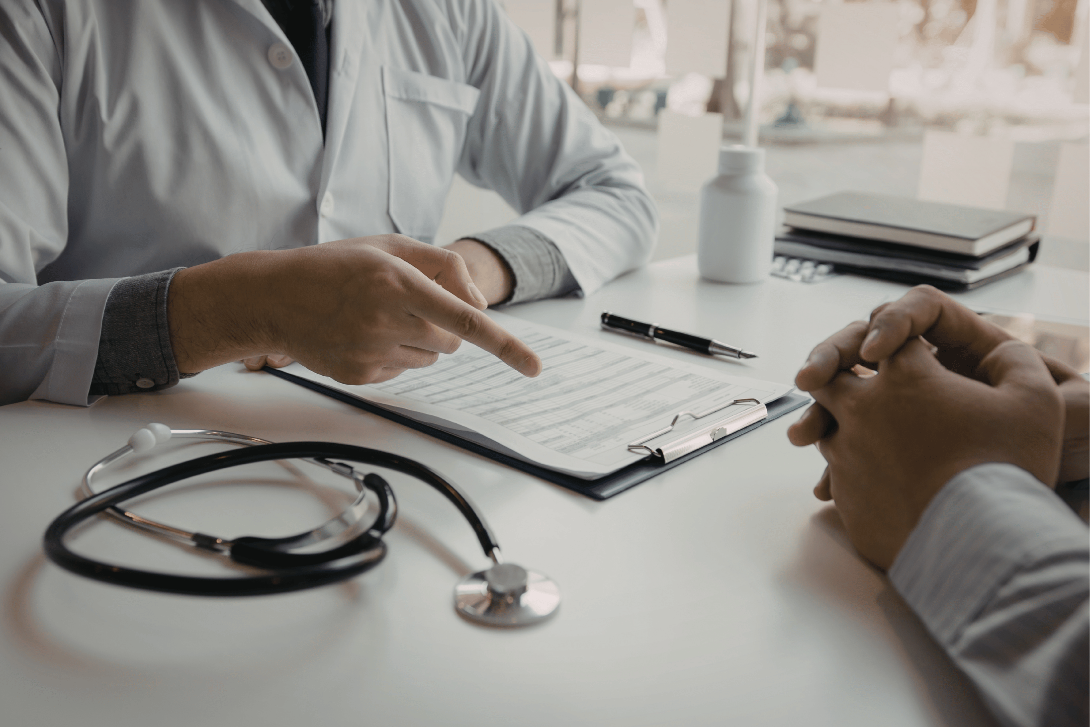 Close-up photo of a doctor and patient's hands over a desk, having a discussion