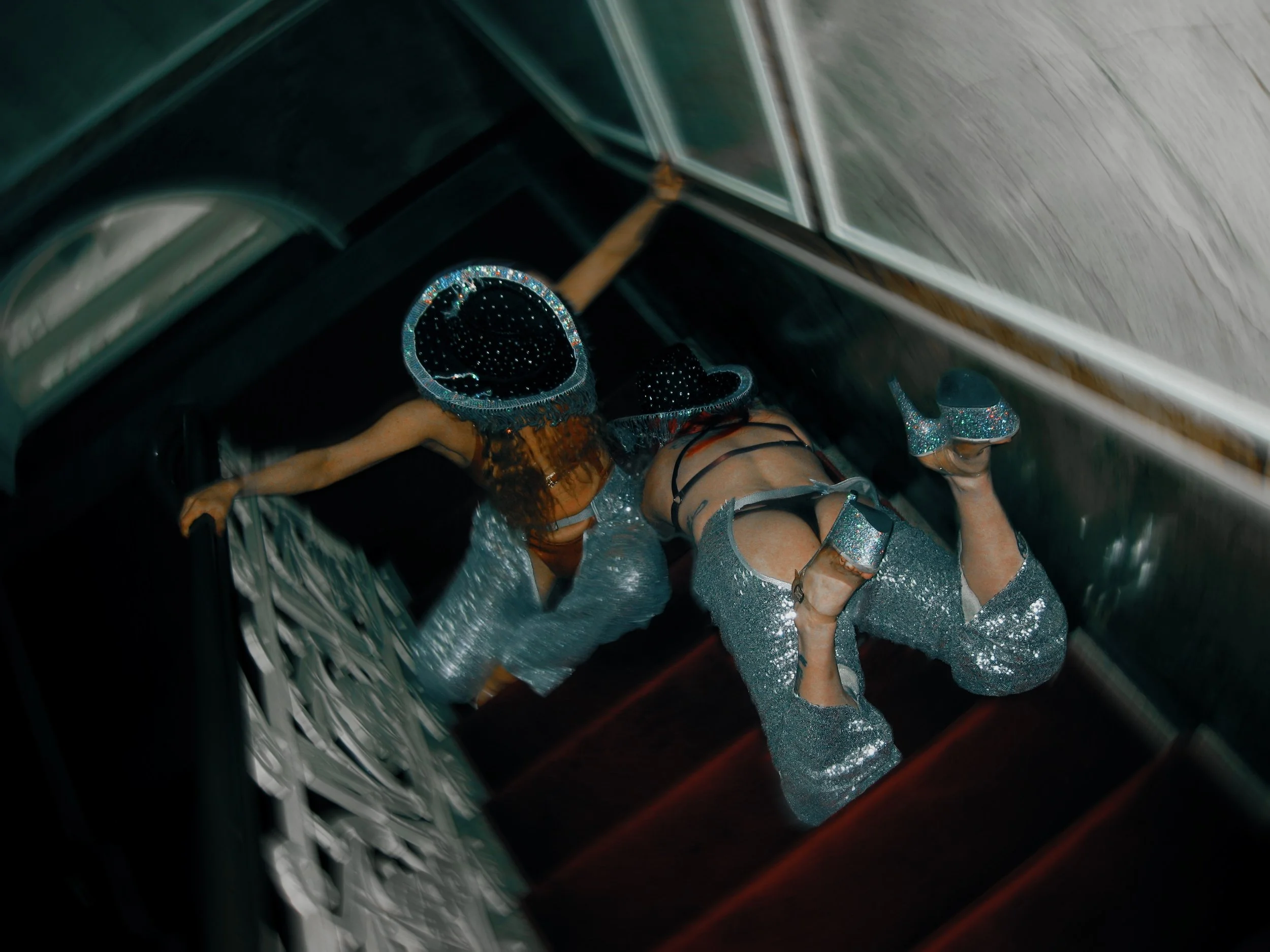 Woman in a sparkling silver outfit and glittery platform shoes climbing a staircase with a mirrored wall on the side, viewed from above.