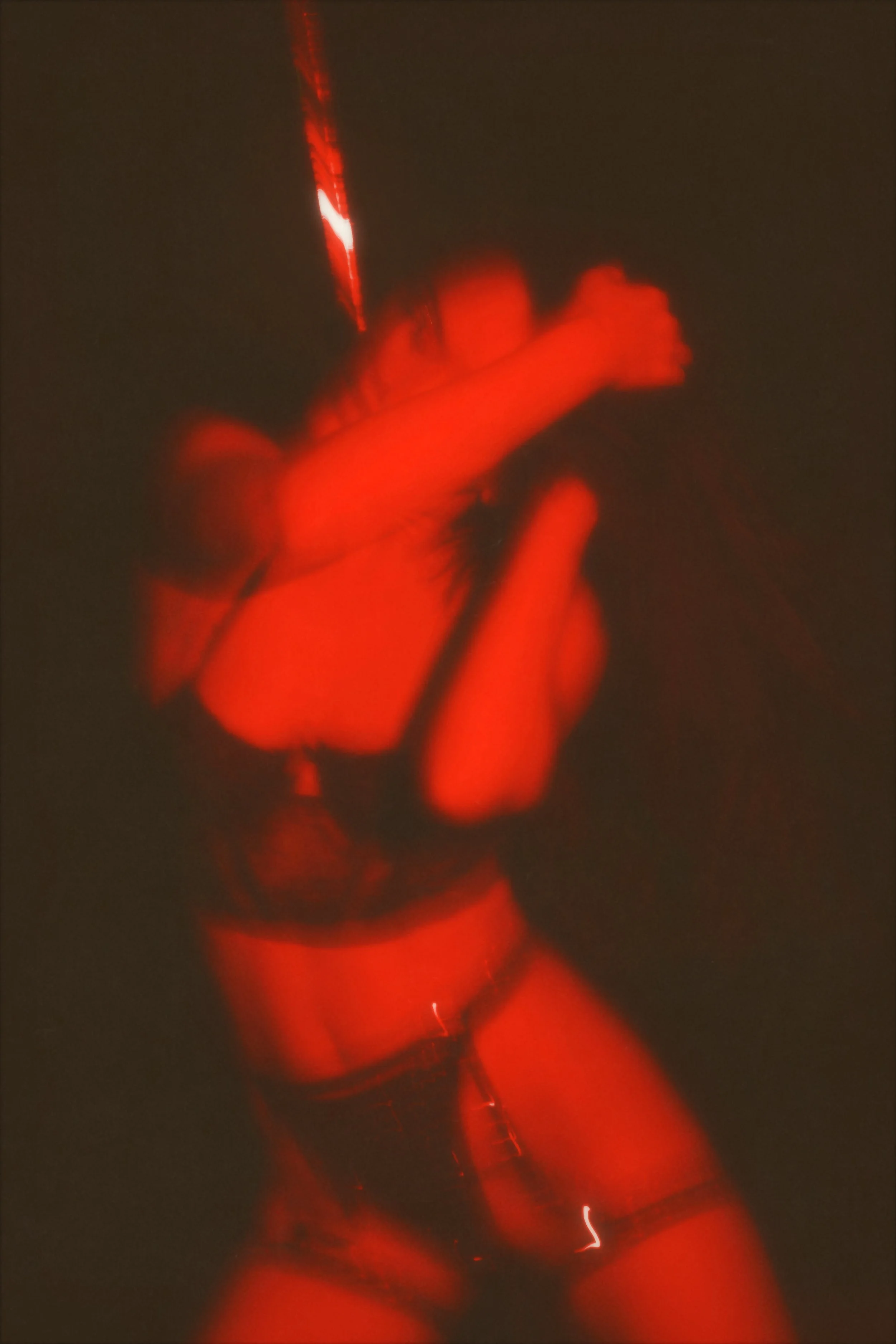 Henkilö poseeraa vähäisissä vaatteissa, valaistus on tummasävyinen ja punainen.