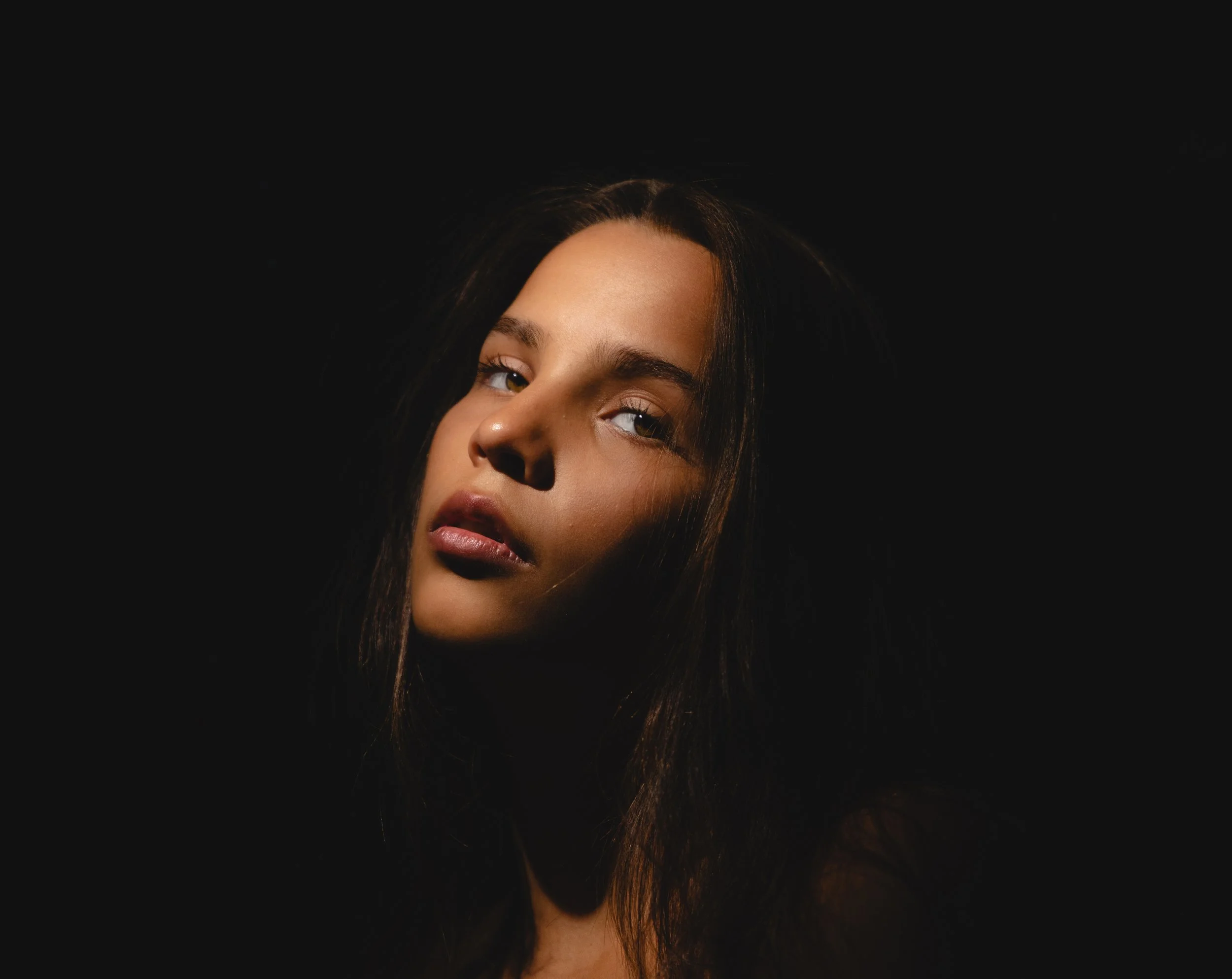 Portrait of a young woman with long dark hair and light skin against a black background.