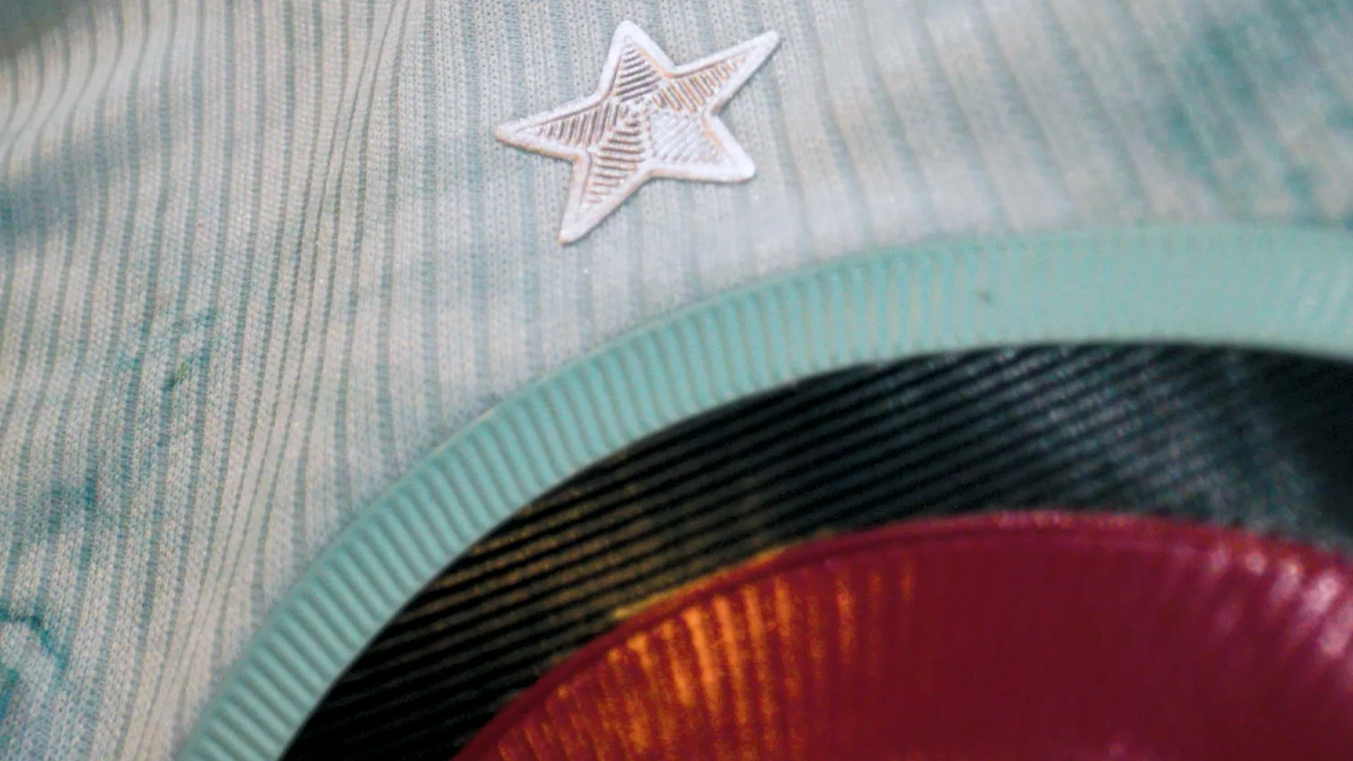 Close-up of a fabric with a small star-shaped embellishment, parts of a red, black, and light blue items are visible.