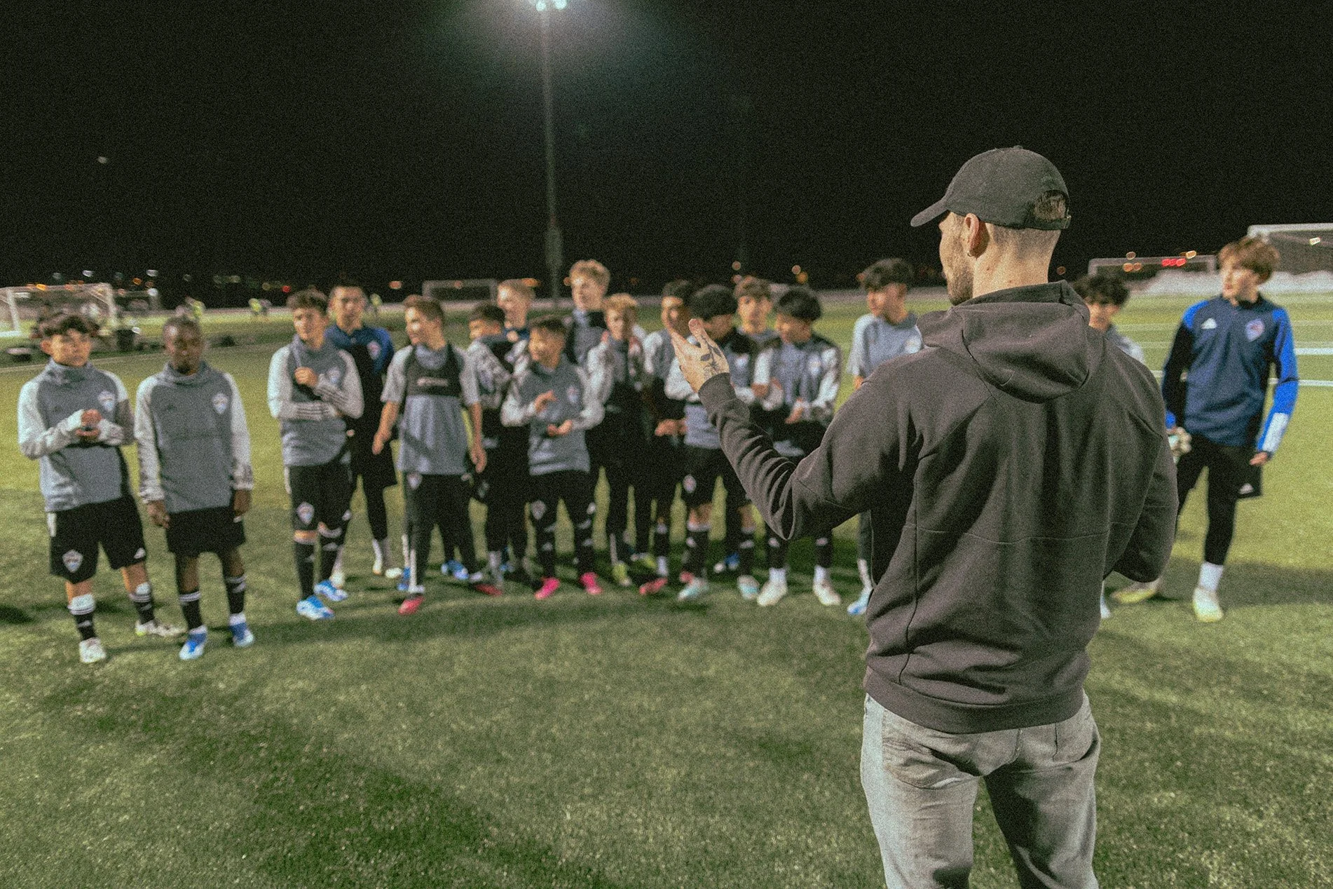 A coach or trainer giving instructions to a youth soccer team on a field at night.