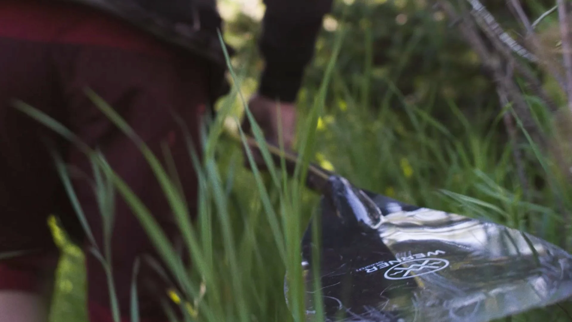 A person wearing dark clothing and red gloves filling a black water bag with water near green grass and trees.